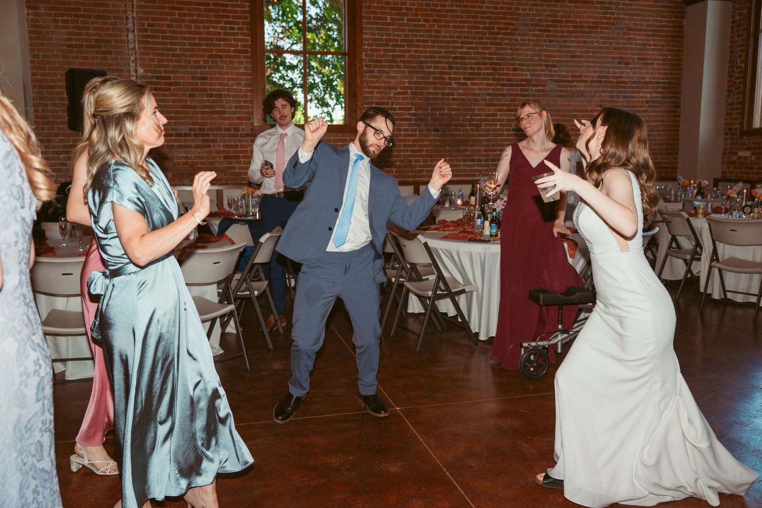 Wedding guests dance and celebrate in a brick venue decorated with string lights.