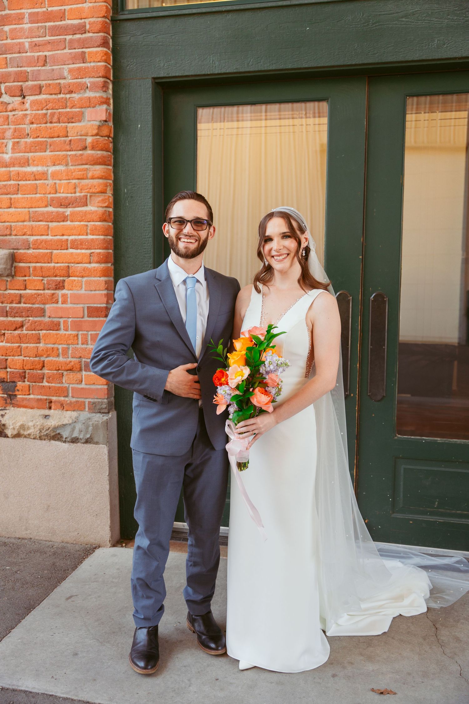 Wedding portrait in front of brick building with elegant floral bouquet.