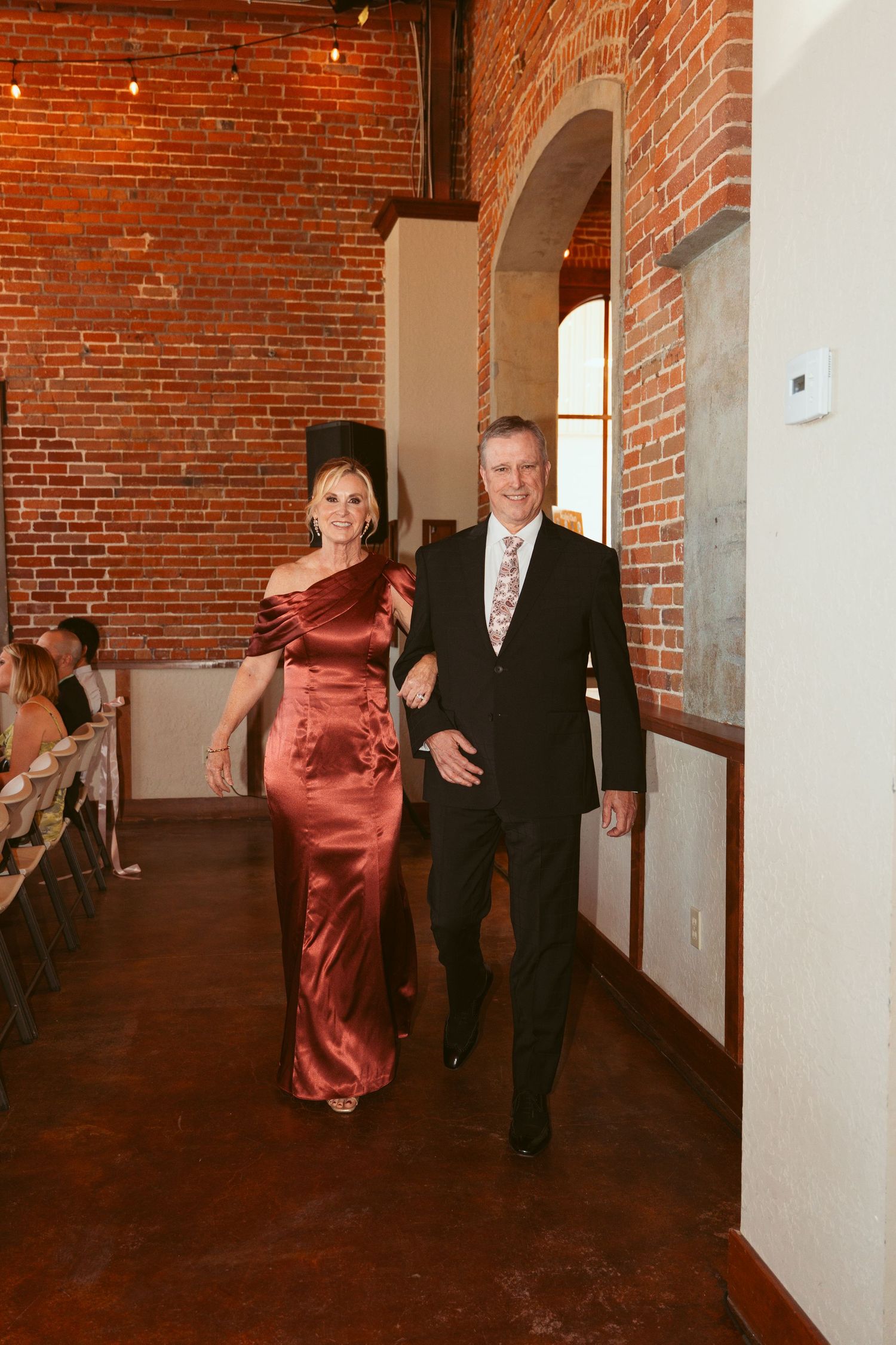 Formal couple walking down hallway with exposed brick walls at elegant event venue.