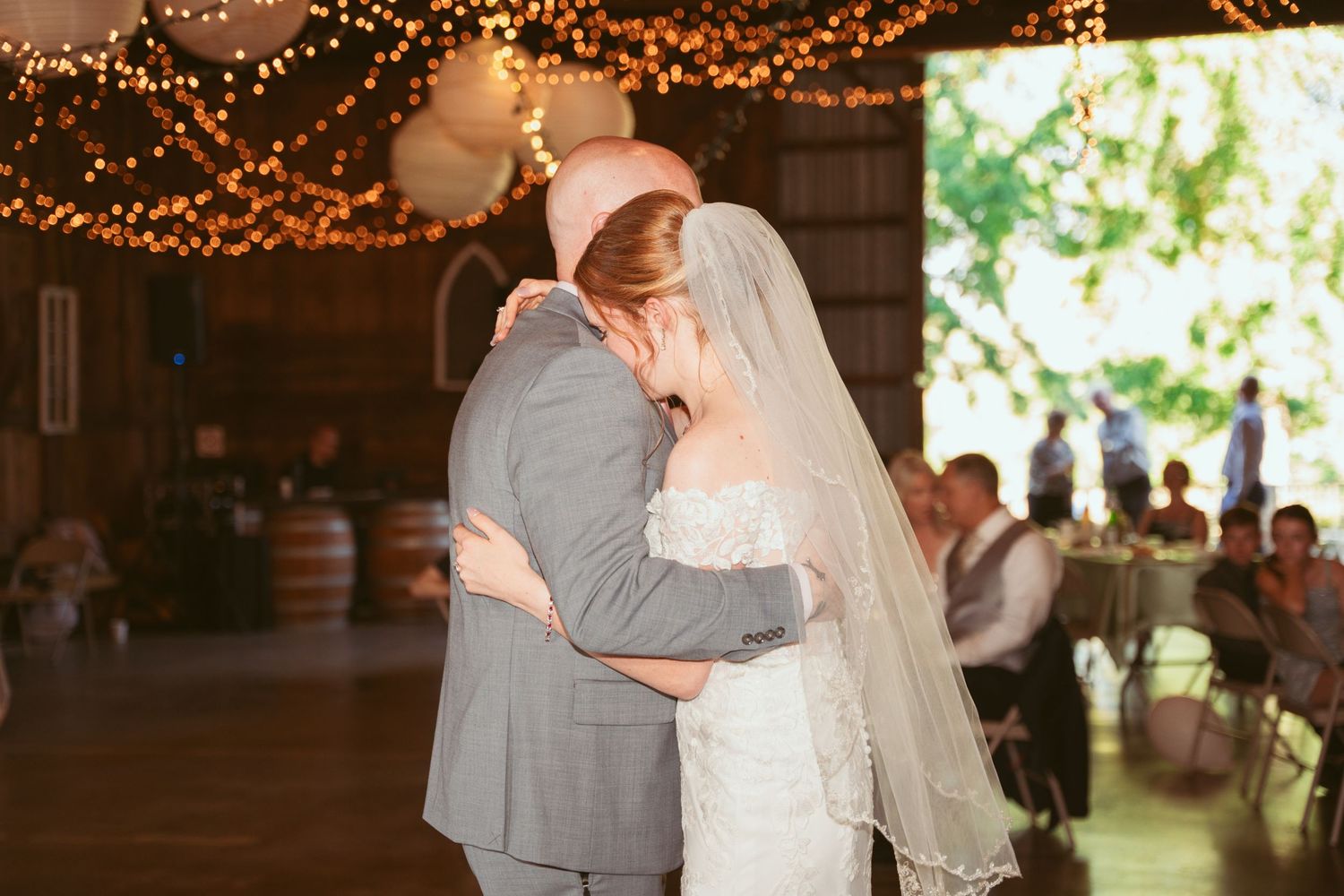 A tender moment between a couple dancing in a beautifully lit barn with paper lanterns overhead.