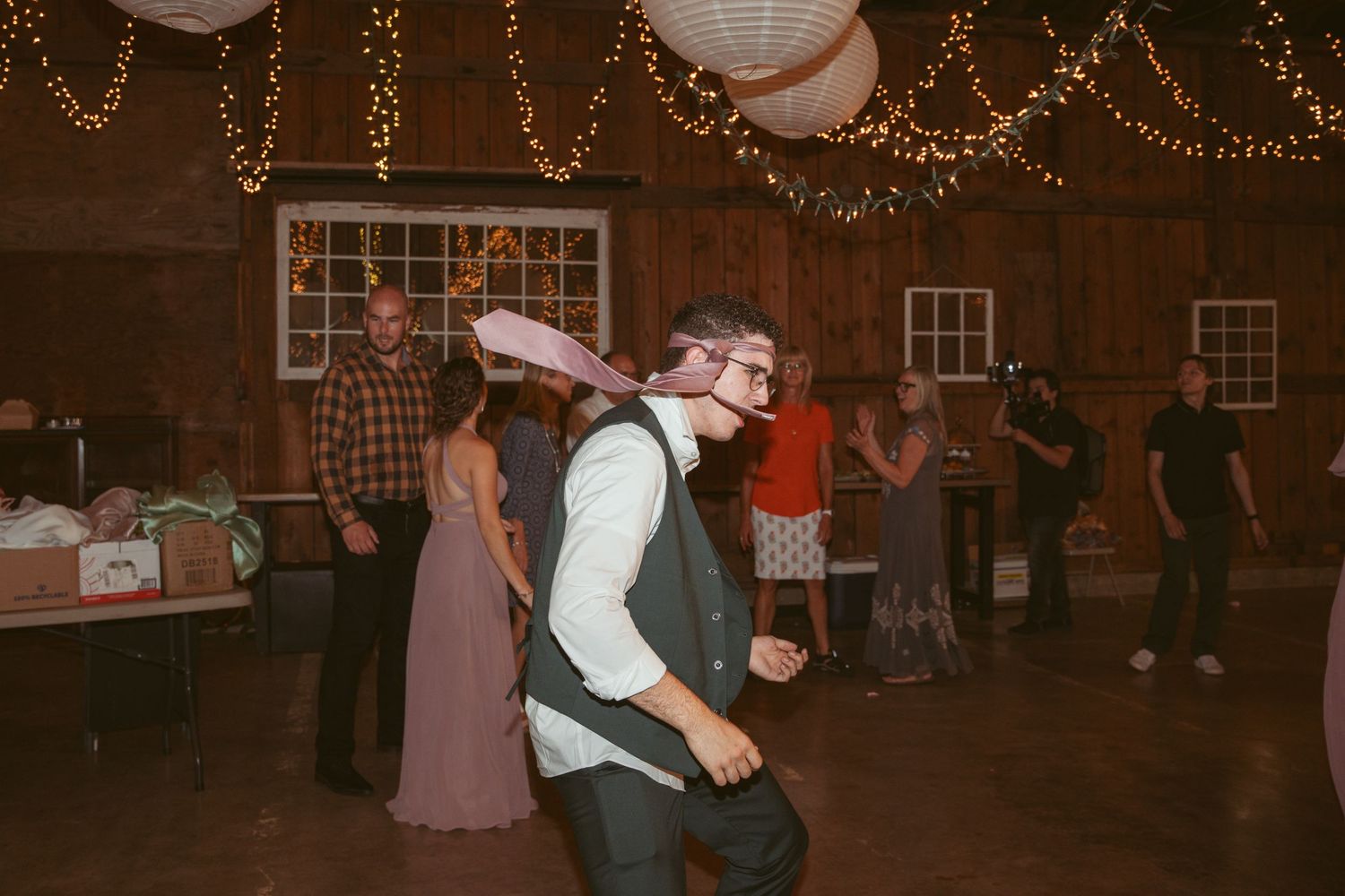 Wedding celebration with guests dancing under warm lighting in a rustic indoor venue.