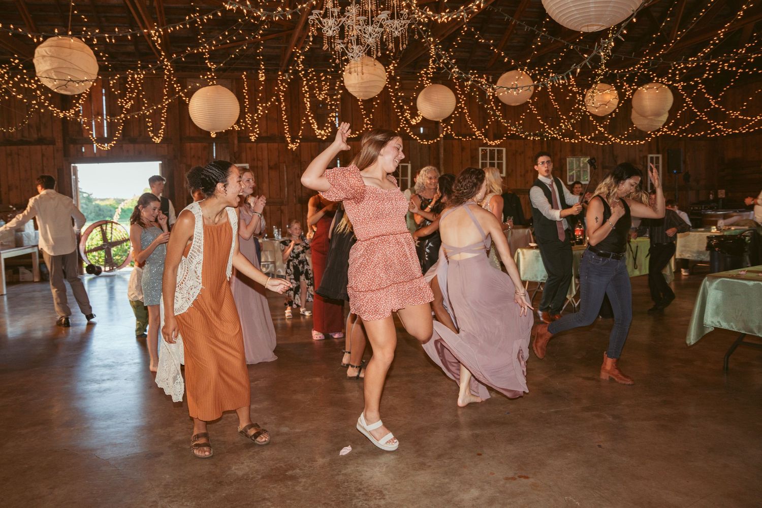 Lively dance floor scene with guests in formal wear under romantic string light decorations.