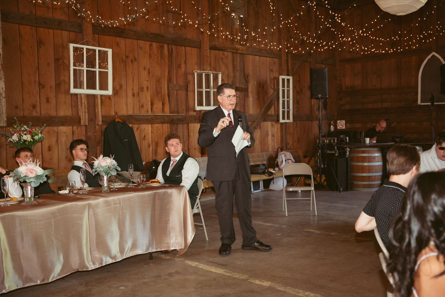 Wedding reception in progress inside a beautifully lit historic barn venue.