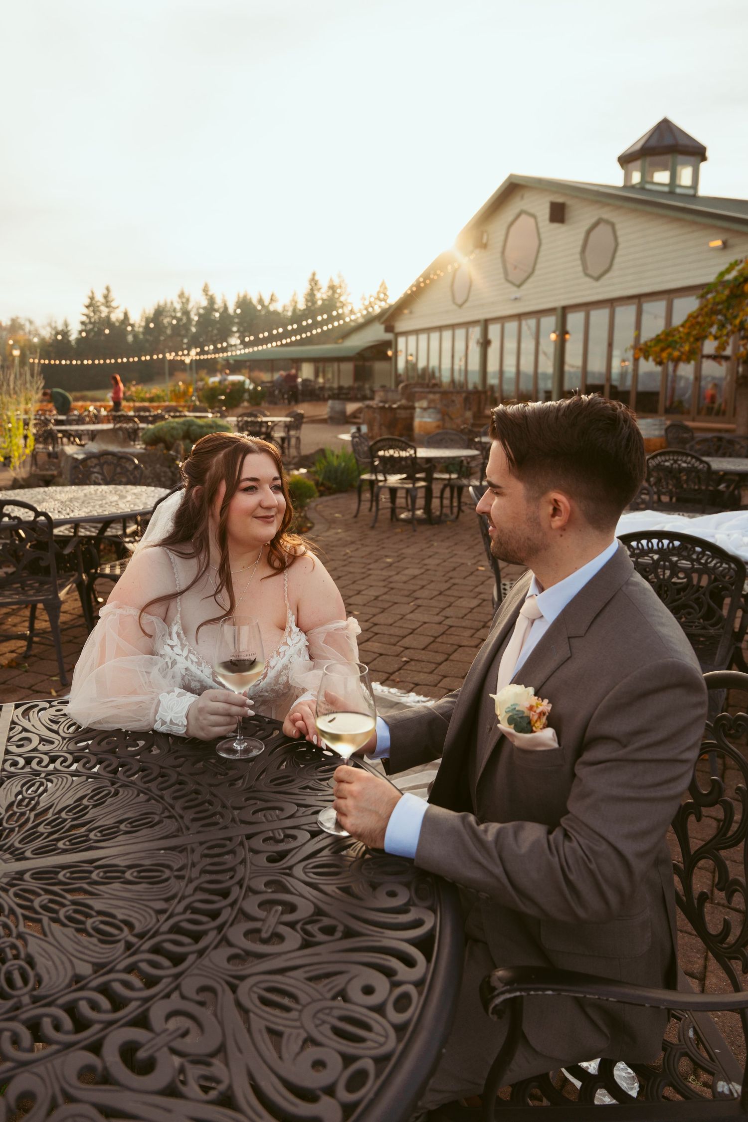 Newlyweds share a romantic moment at sunset on an outdoor patio with string lights and mountain views.