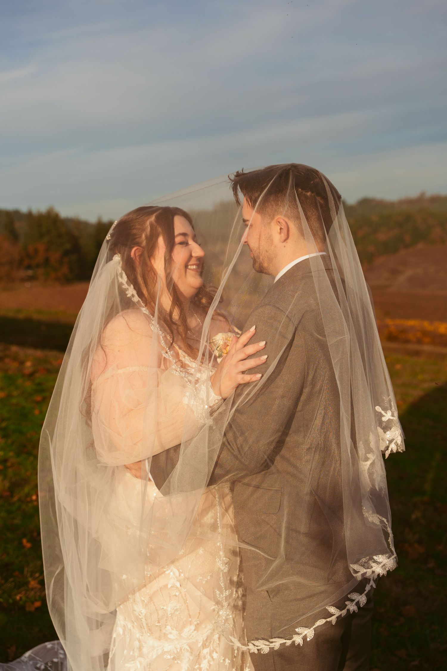 A couple shares a joyful moment under a wedding veil in autumn sunlight.