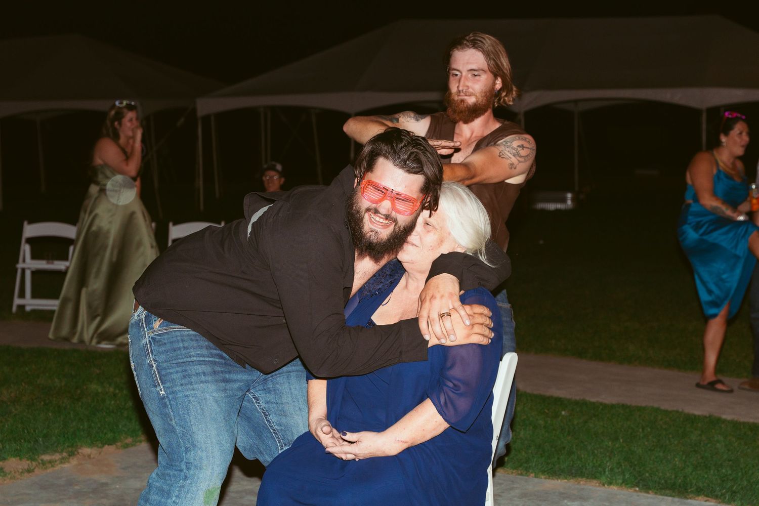 Wedding guests dancing under evening lights at an outdoor barn reception.