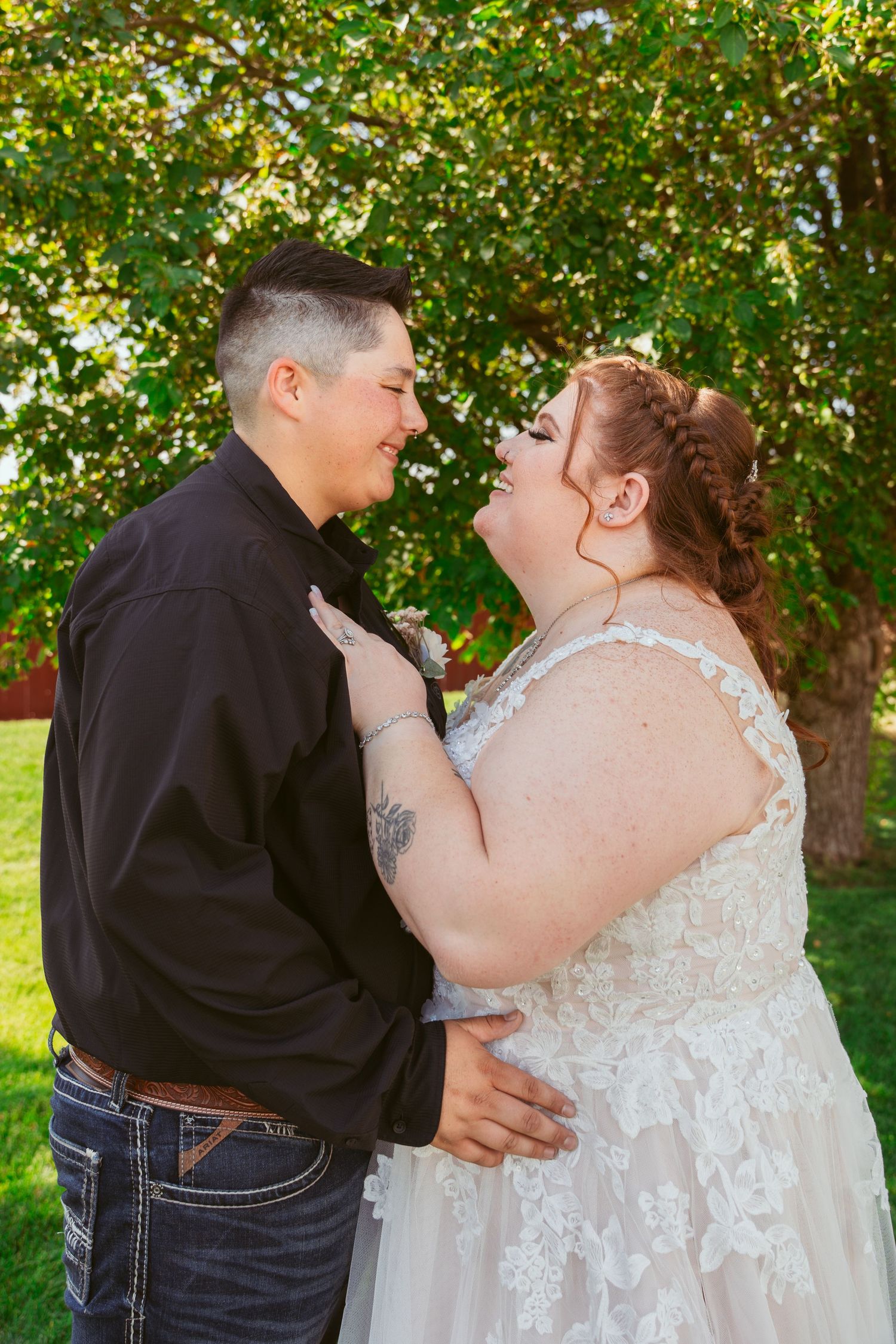 A romantic wedding couple shares an intimate moment in a garden setting with green trees in the background.