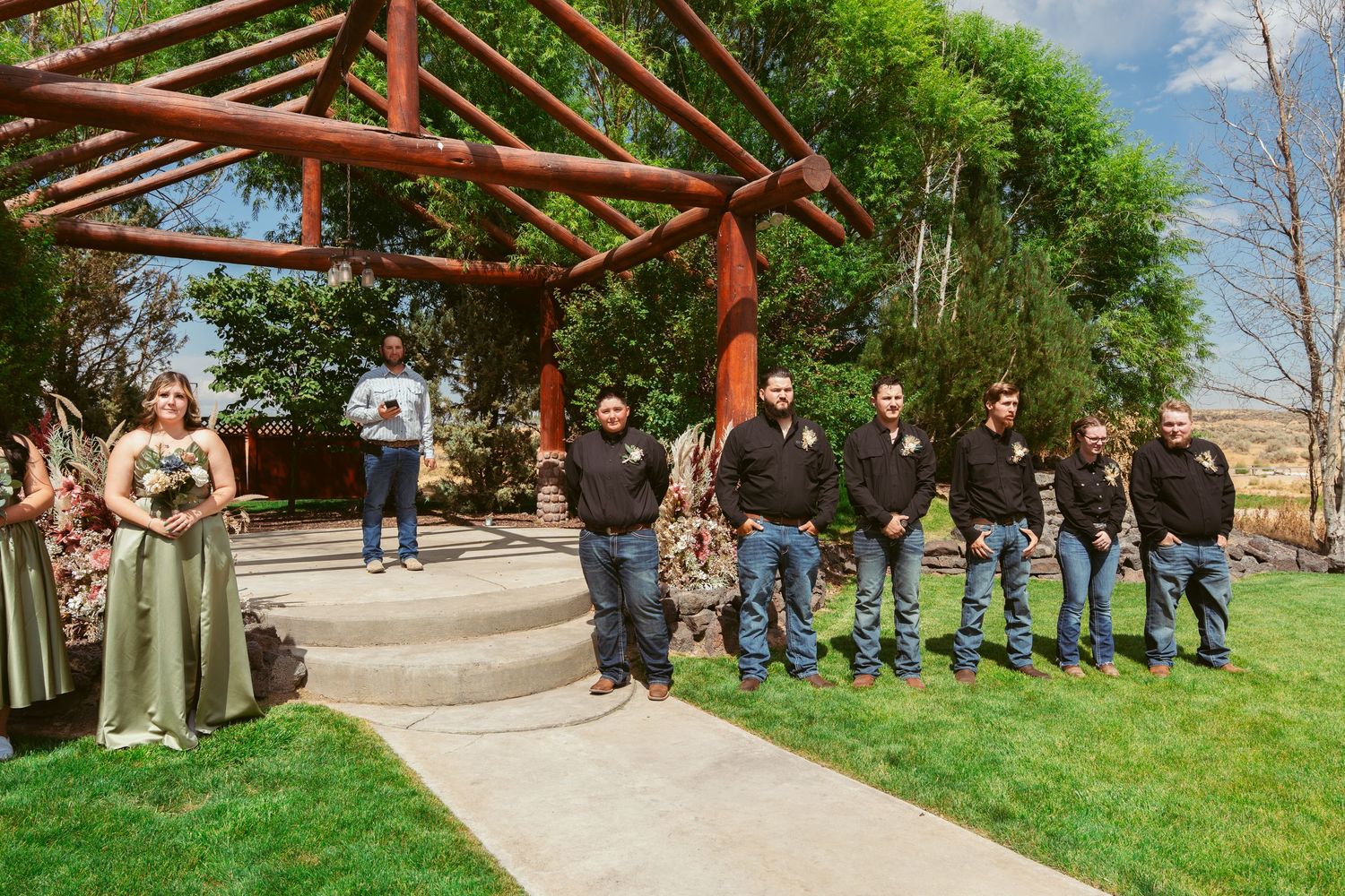 Wooden pergola structure set up for outdoor wedding ceremony with guests seated on white chairs.