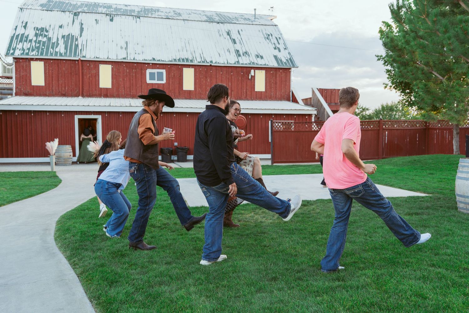 People performing choreographed dance moves on grass near a red barn.
