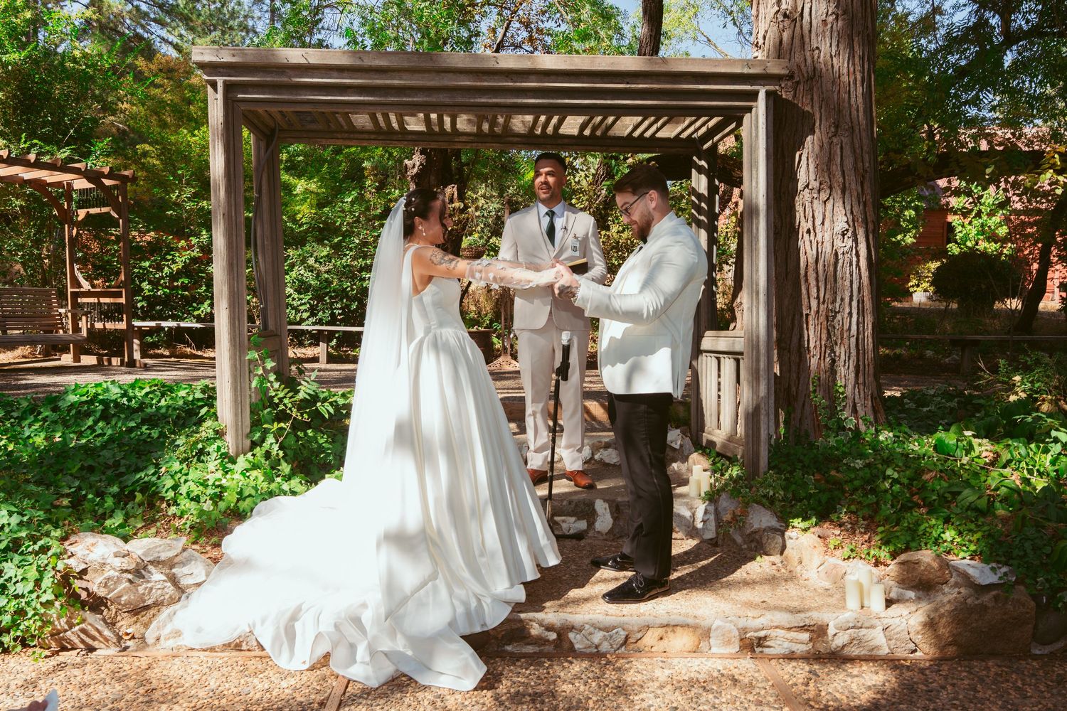 Elegant wedding photos taken under rustic wooden pergola in a lush garden setting.