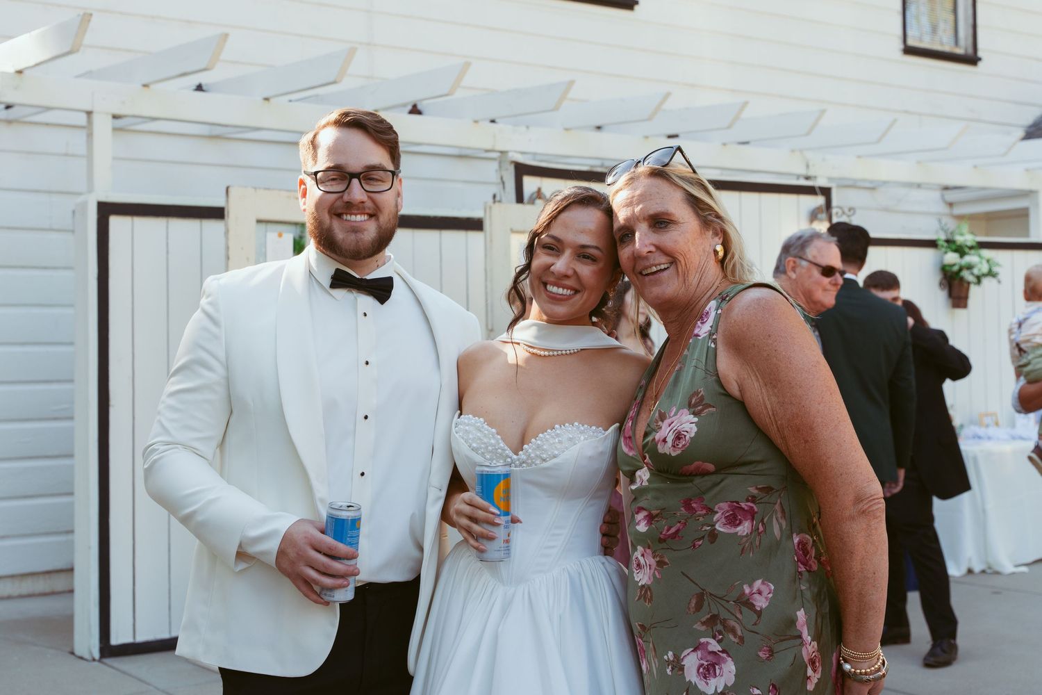 Wedding guests in formal attire pose together outside a white building during a celebration.