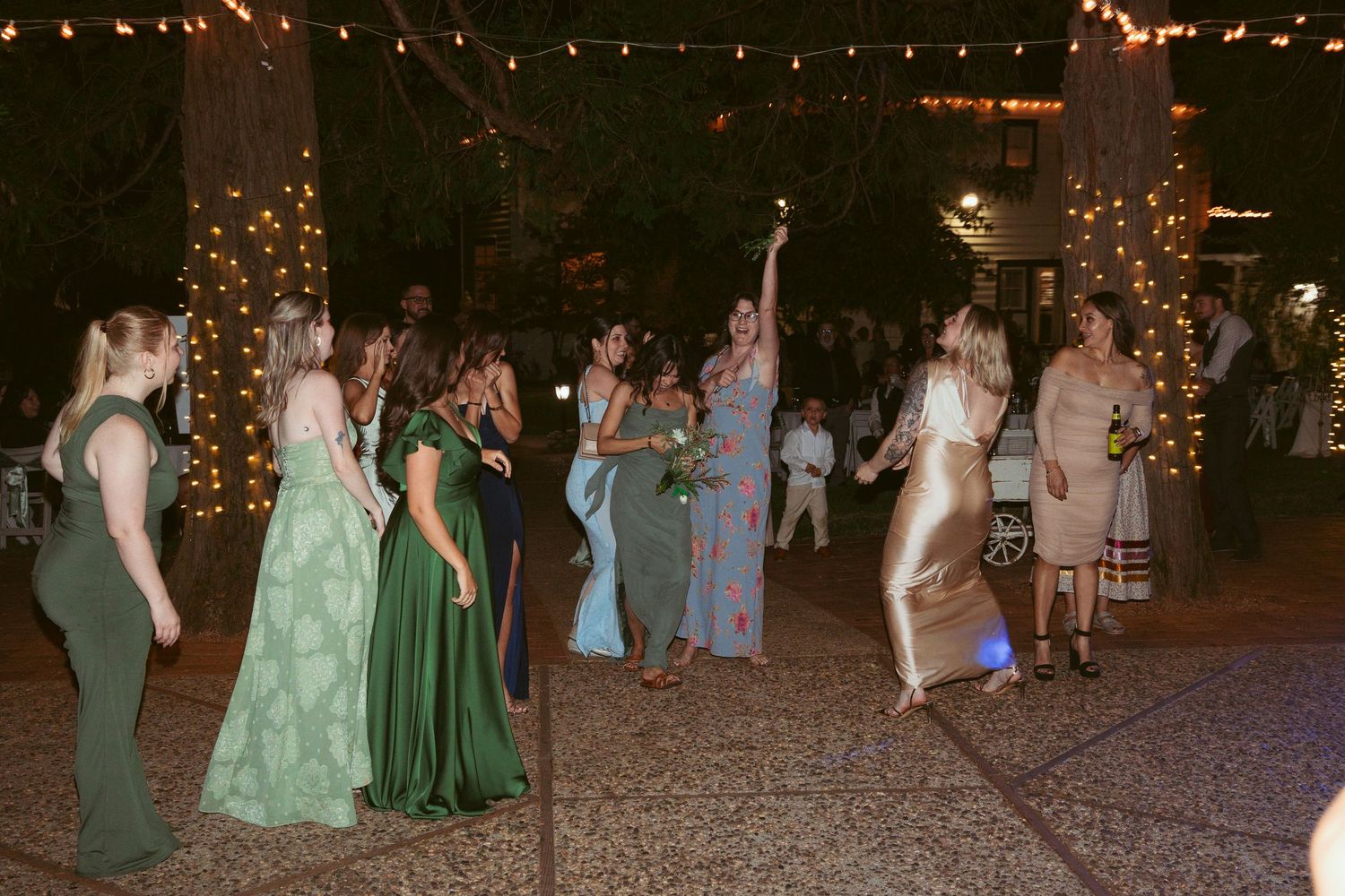Wedding guests dancing together on an outdoor dance floor illuminated by overhead string lights.