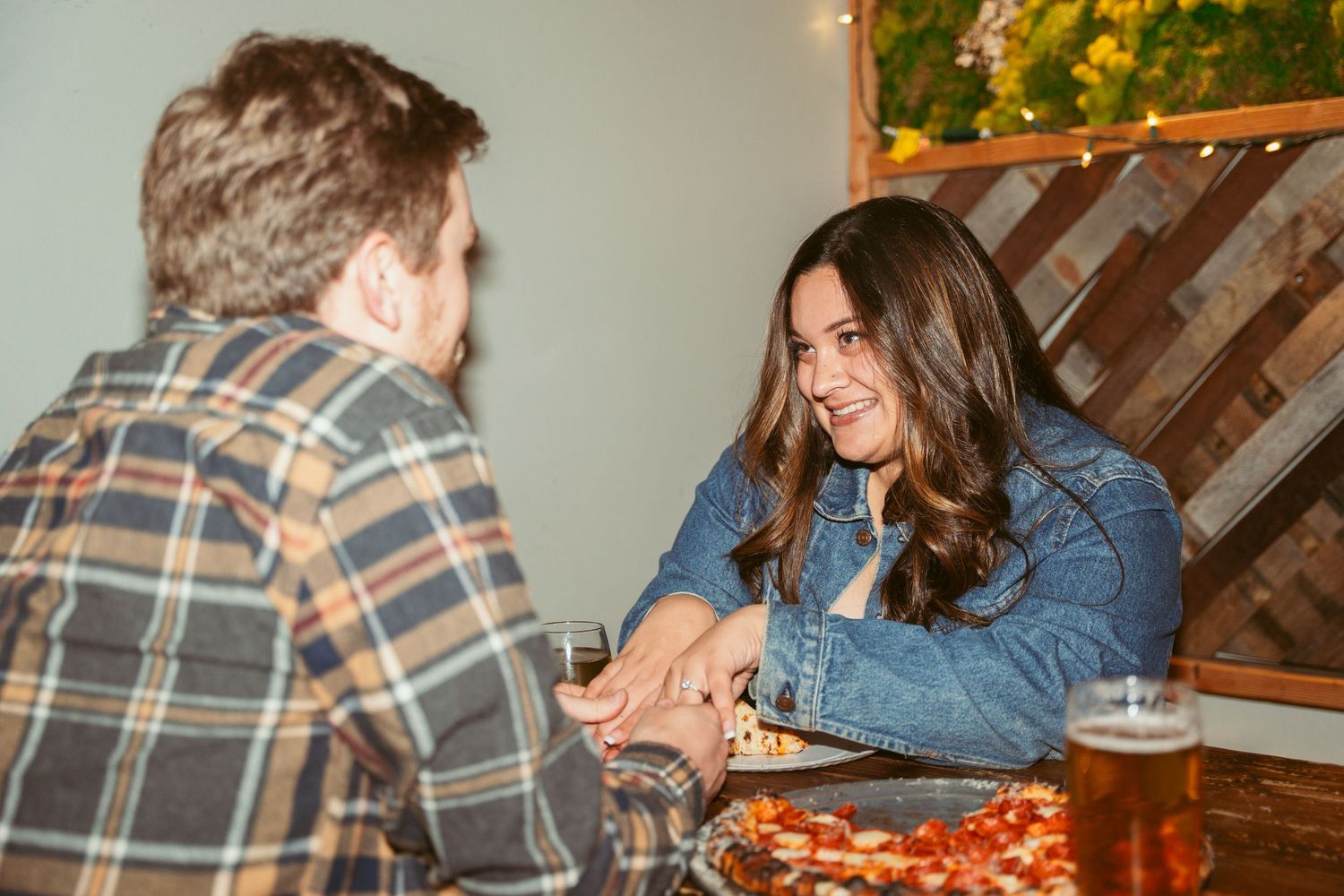 A couple sharing pizza and drinks at a rustic restaurant table in a cozy setting.