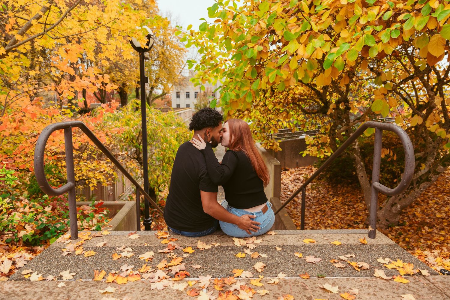 A couple enjoys autumn scenery surrounded by golden leaves and park benches.