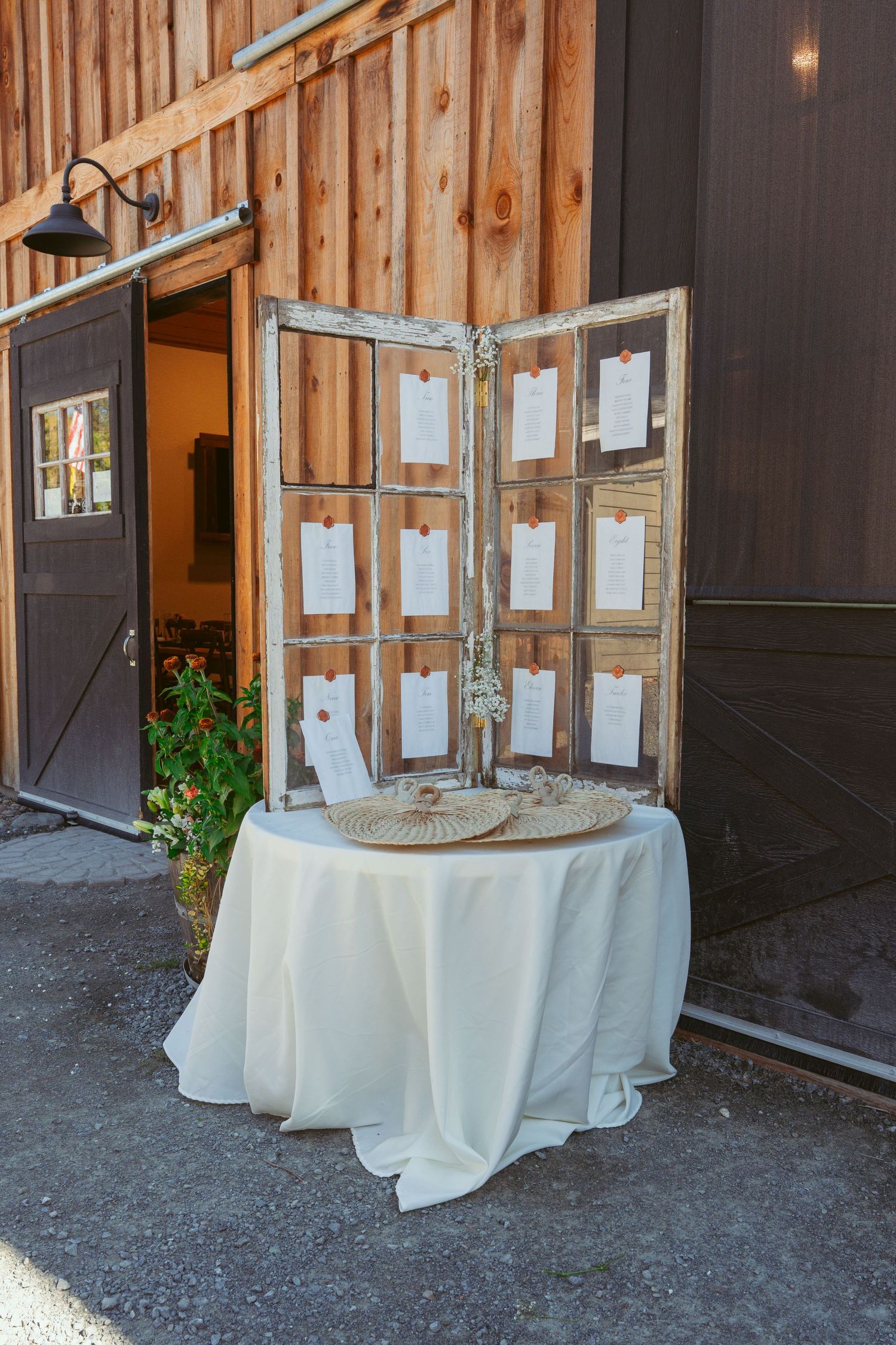 Vintage window frame seating chart display on white tablecloth at rustic barn venue.