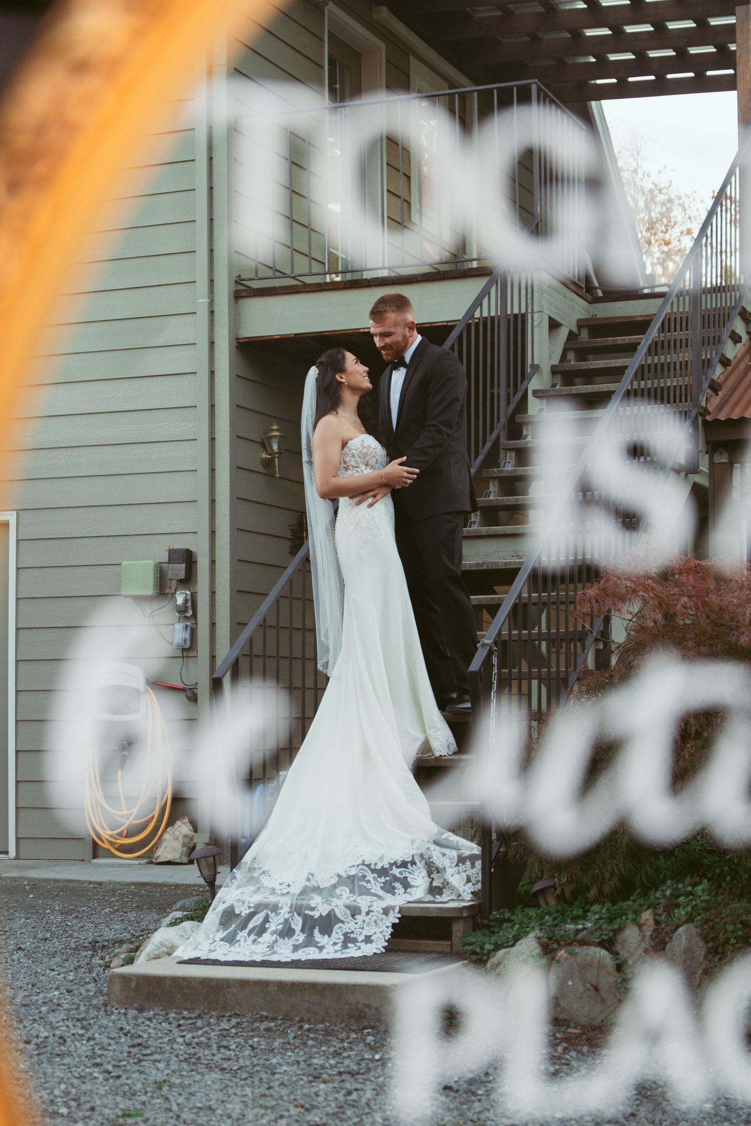 Artistic wedding photo through frosted glass showing couple embracing by staircase.