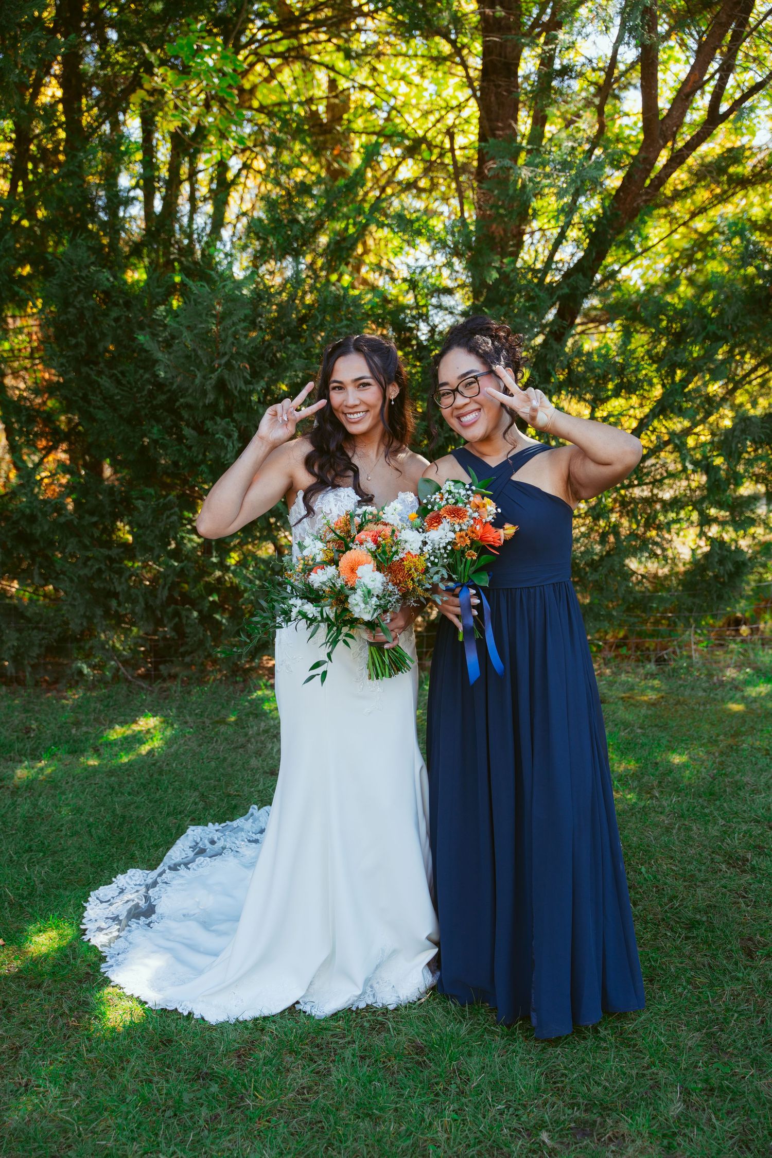 Wedding party in navy blue dresses and white gown pose playfully on grass with vibrant orange bouquets.