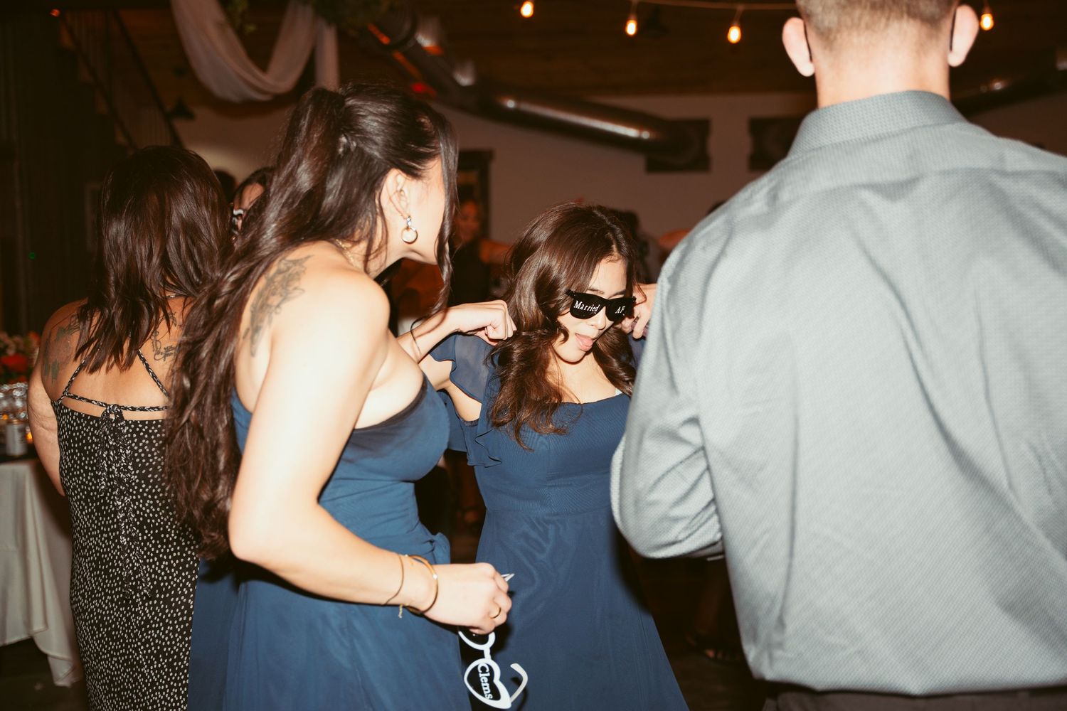 Wedding reception guests dancing and celebrating on dimly lit dance floor.