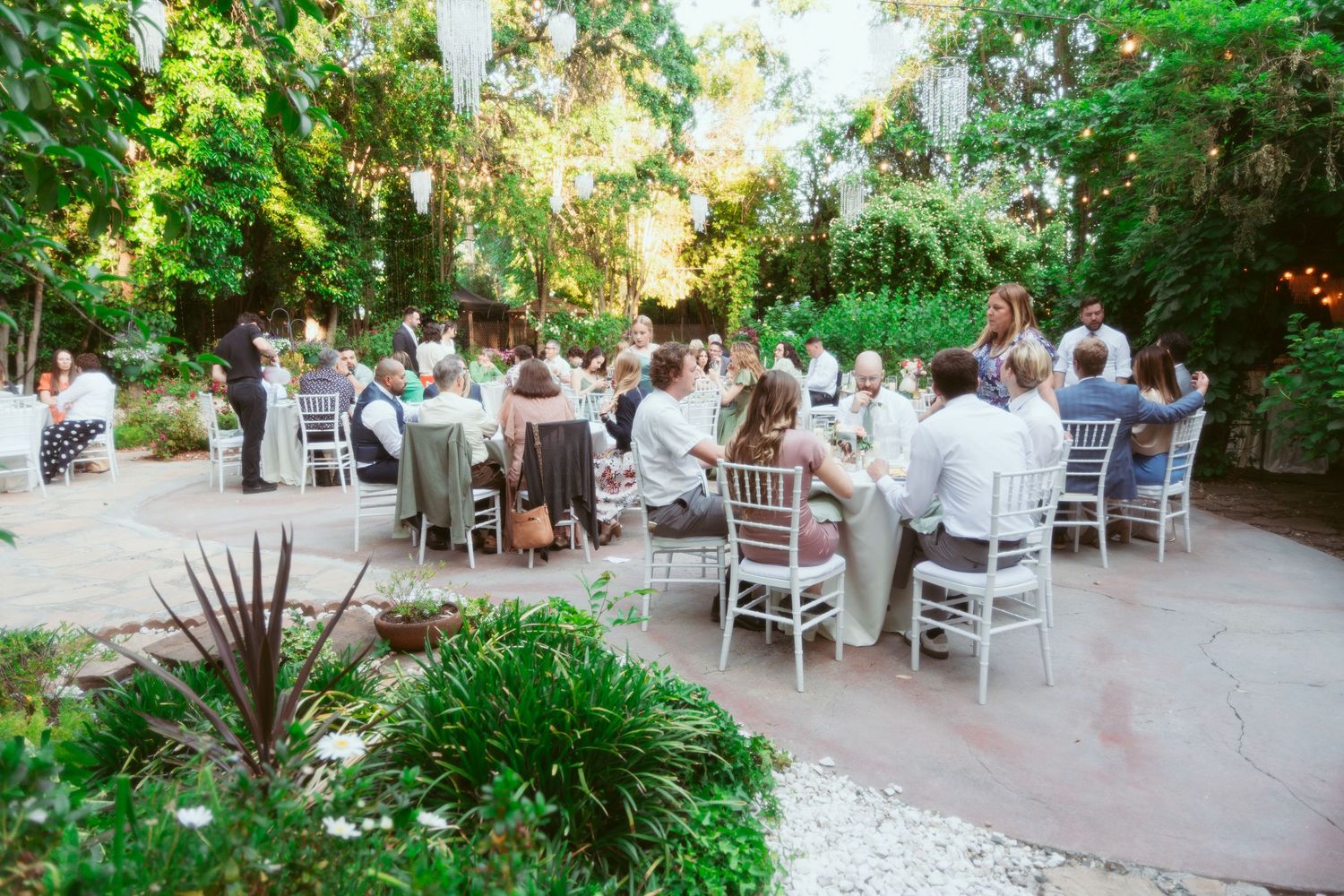 Elegant outdoor wedding reception setup with white chairs and tables in a garden setting.