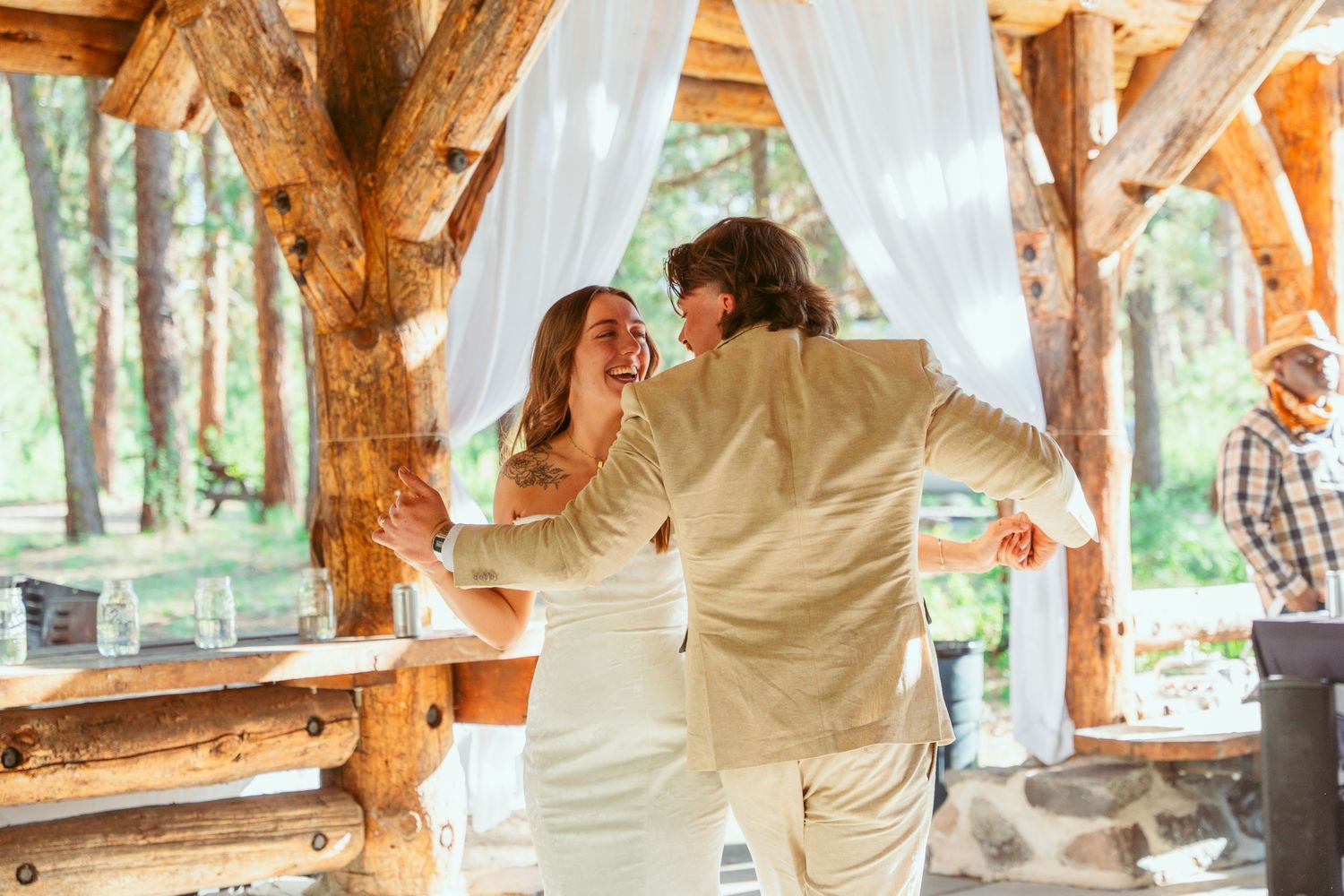 Romantic dance moment under a log-beam pavilion decorated with white fabric and string lights.