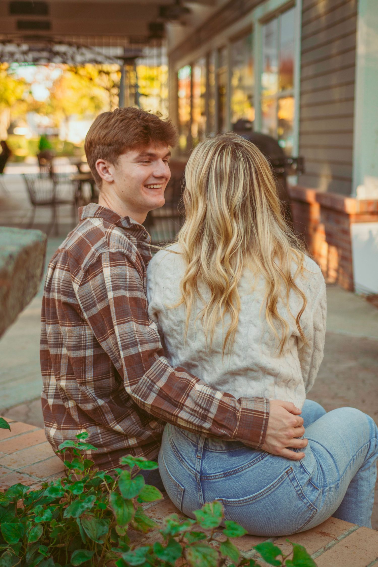 A couple shares an intimate moment on a brick wall during sunset.