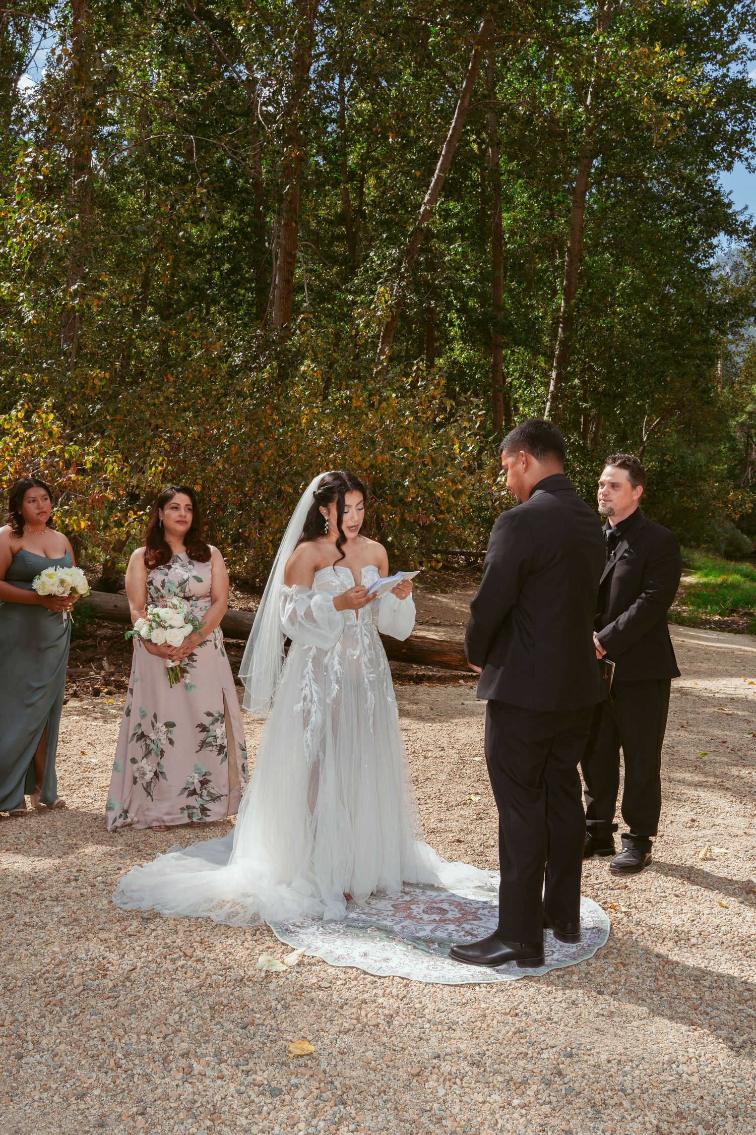 Wedding ceremony group gathered on gravel path surrounded by autumn trees.