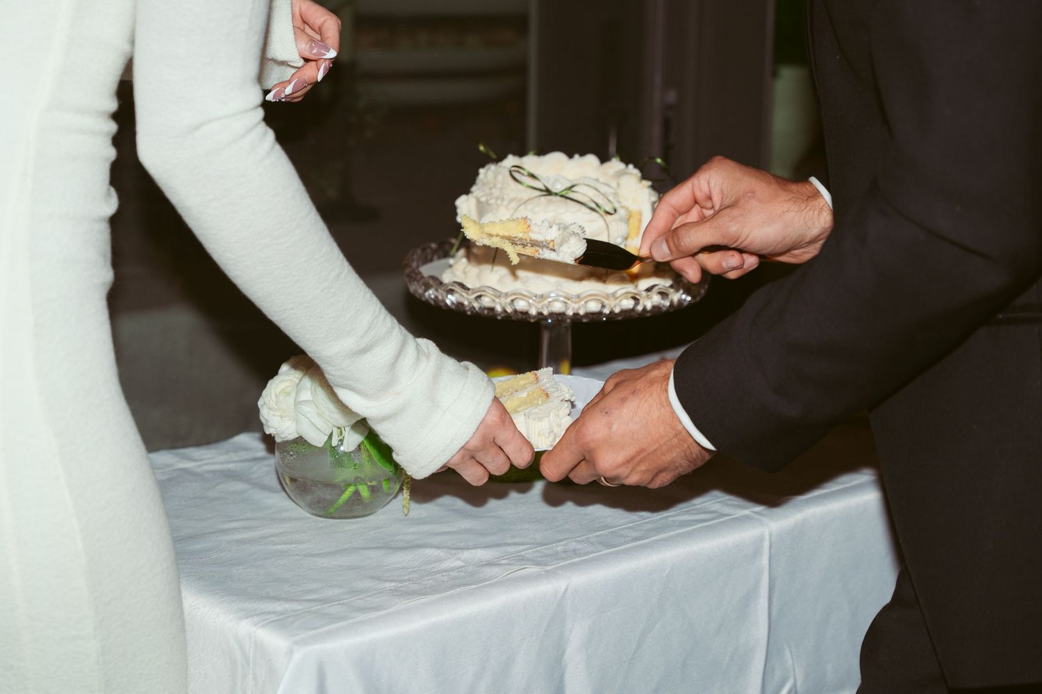 Wedding couple feeding each other pieces of white wedding cake at their reception.
