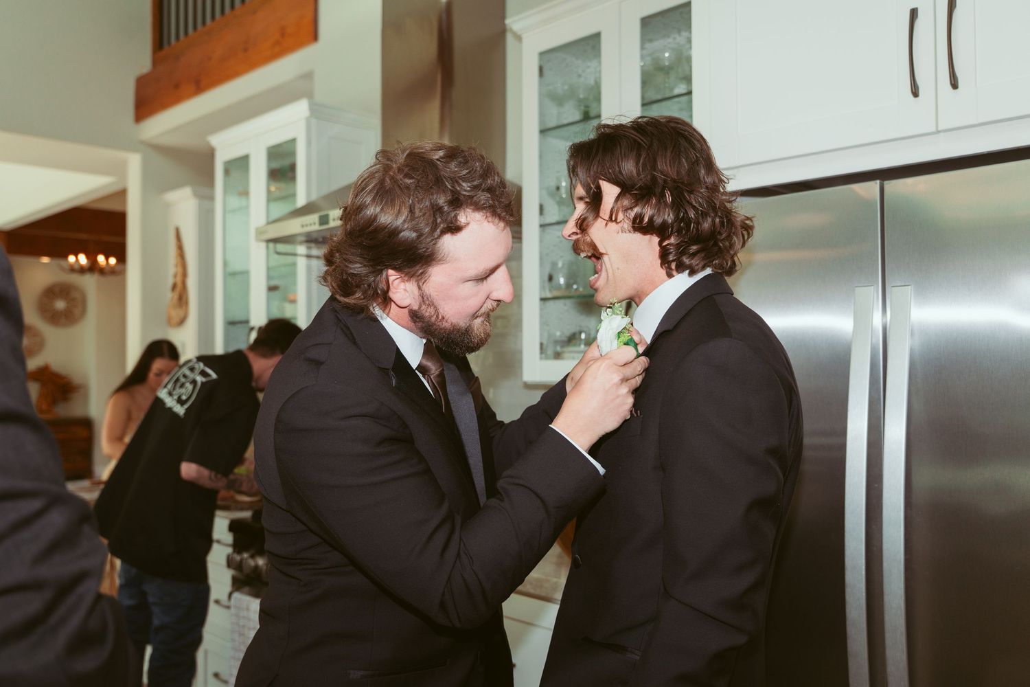 Groomsmen in black suits sharing a celebratory moment in a modern kitchen setting.