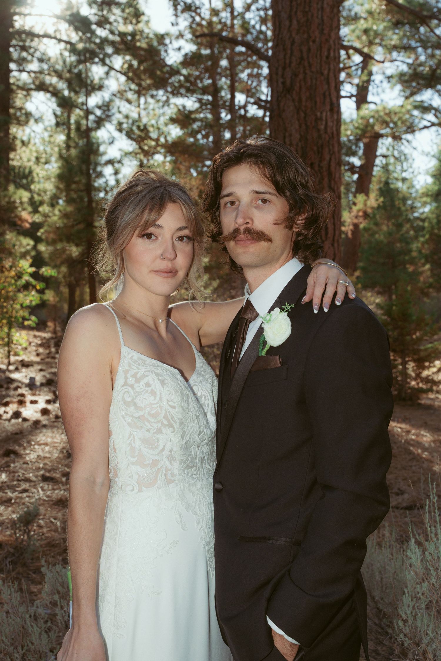 A rustic outdoor wedding portrait with pine trees and natural lighting.