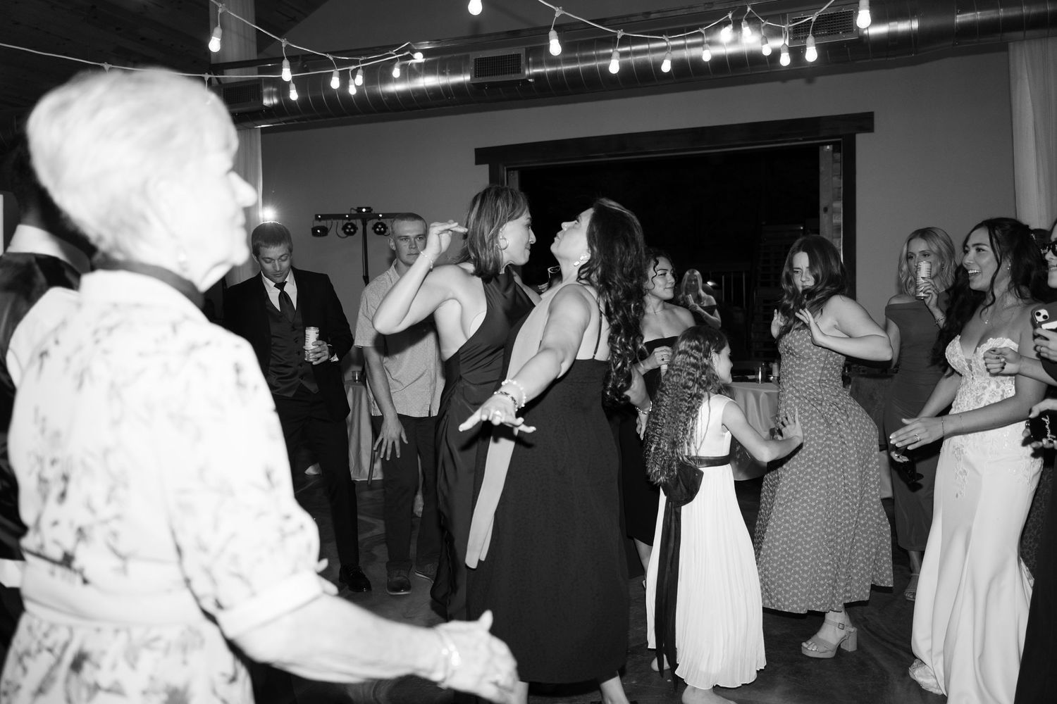 Wedding party and guests dancing enthusiastically at a dimly lit indoor reception.
