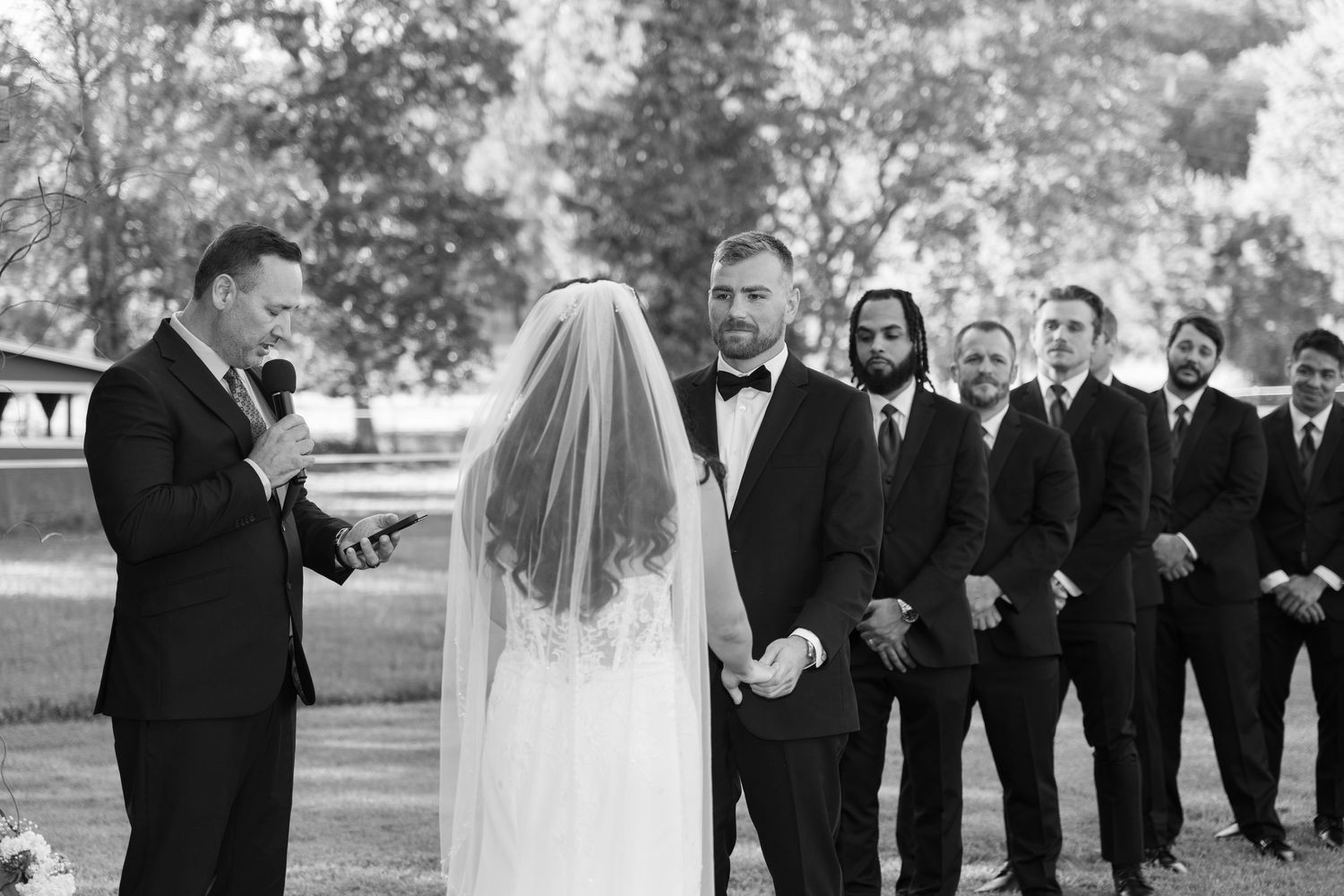 Wedding party in formal attire poses together outdoors on a sunny autumn day.