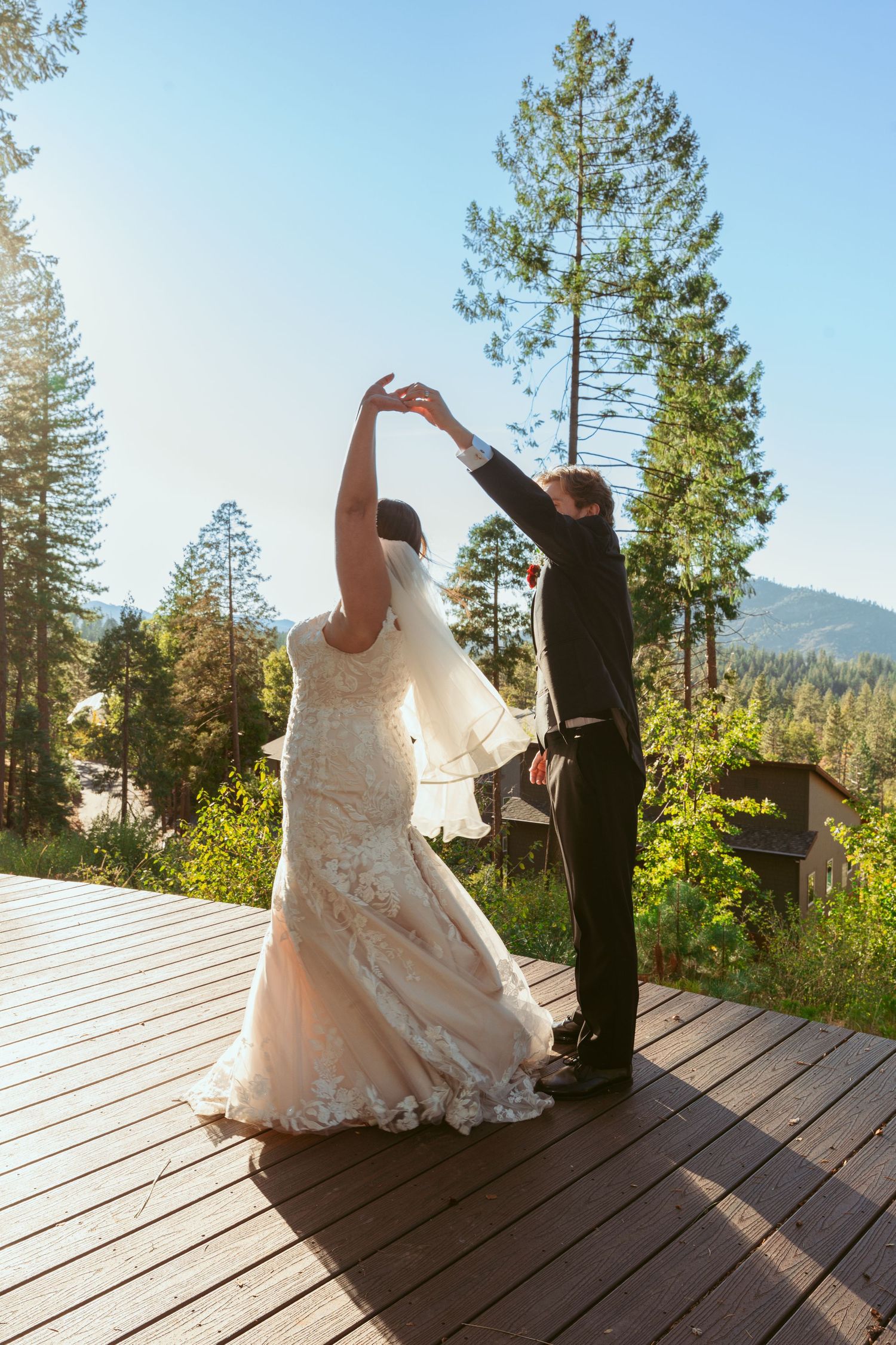 Couple dancing on a wooden deck with mountain views and towering pine trees in the background.