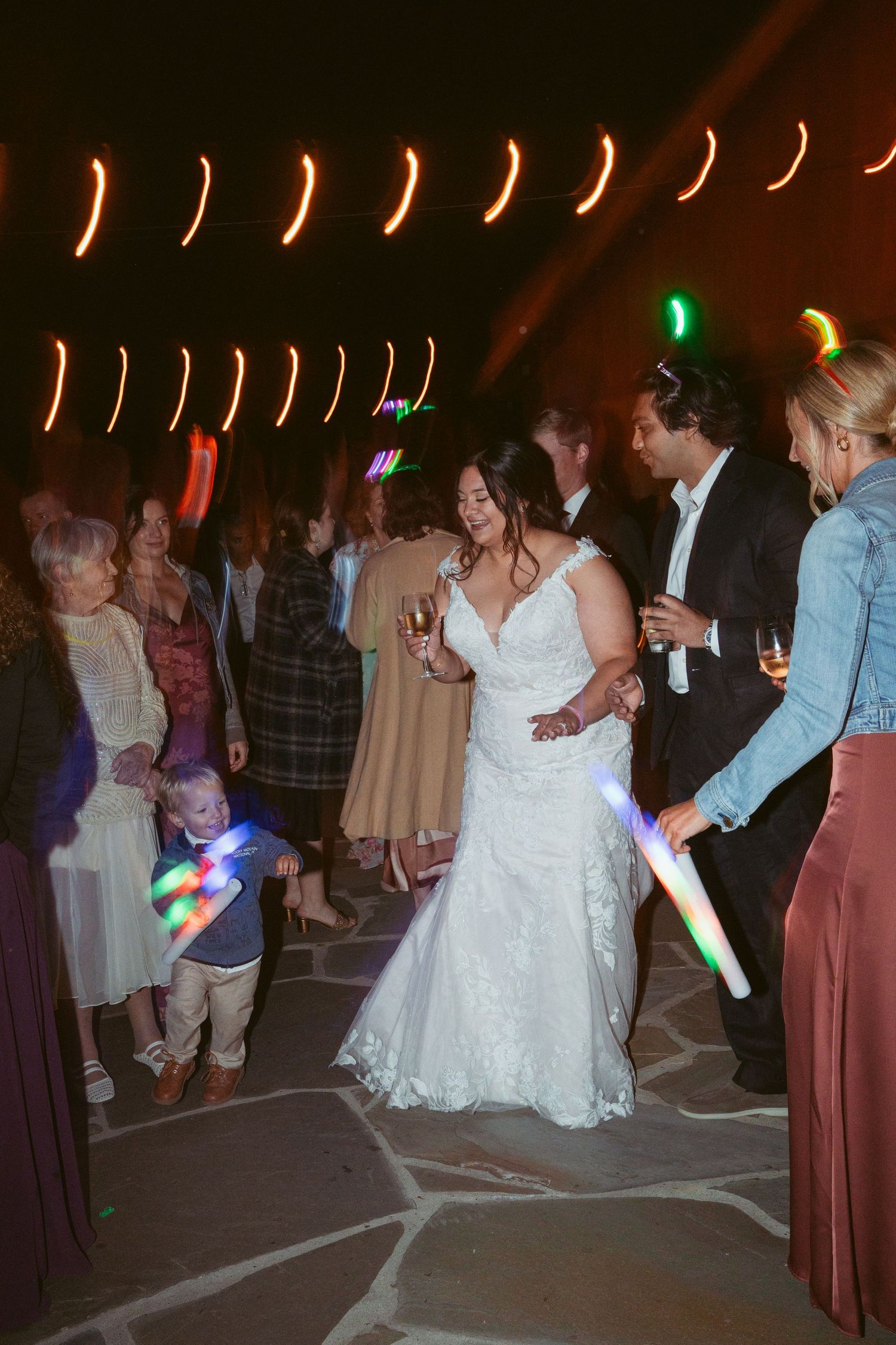 Evening wedding reception with colorful lights and dancing guests on stone patio.