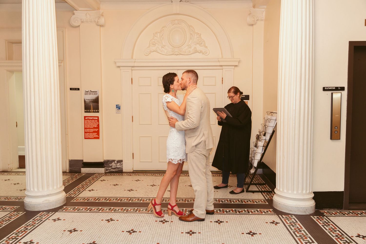 A wedding ceremony taking place in an elegant room with white columns and patterned flooring.