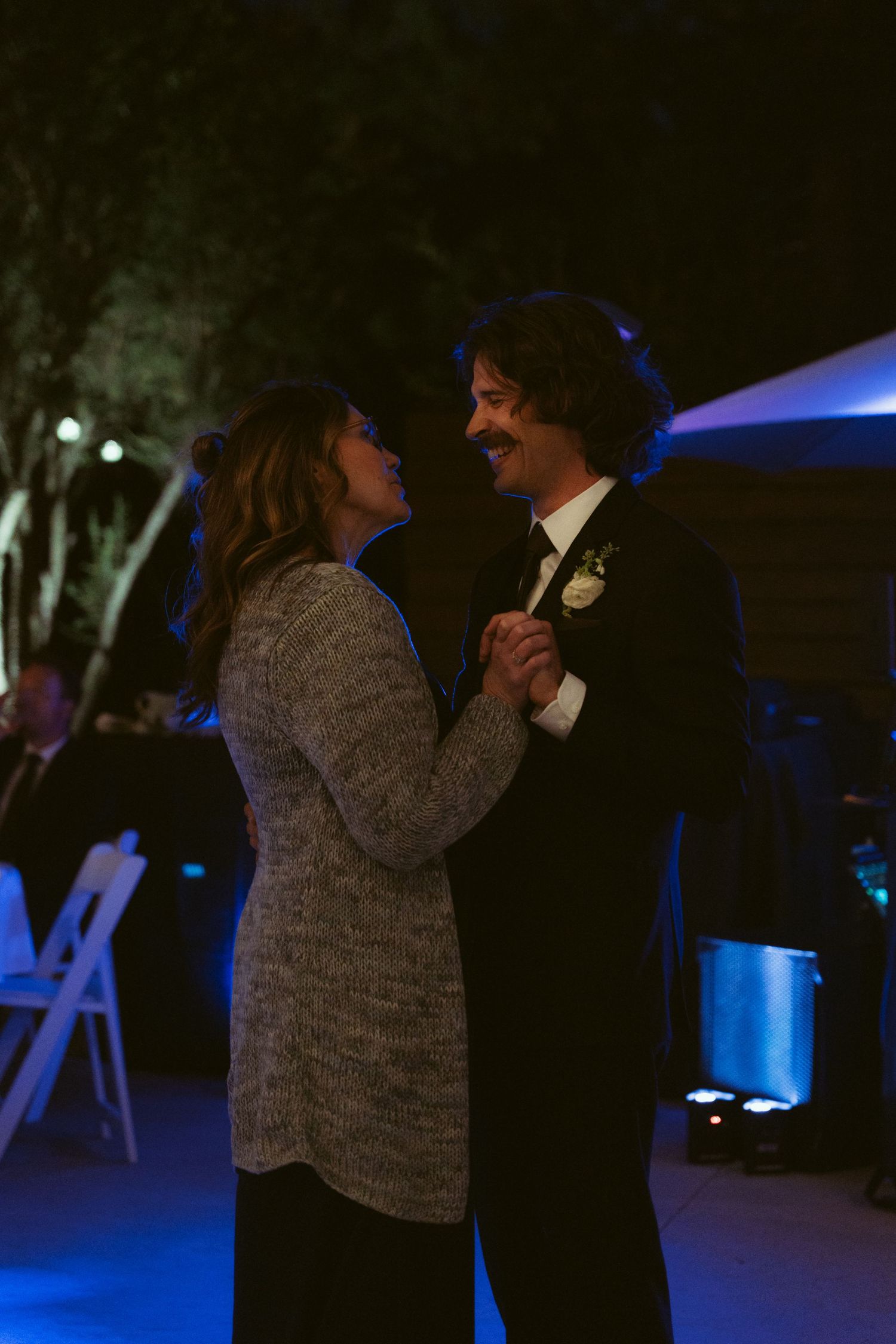 A couple shares an intimate slow dance under blue lighting at an outdoor evening reception.
