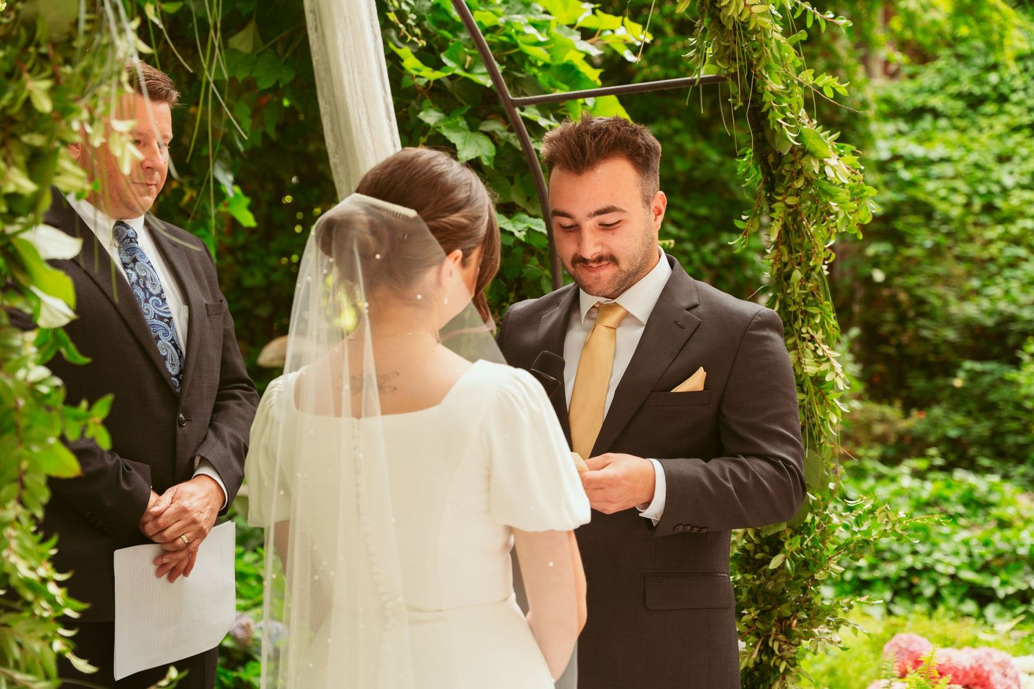 Outdoor wedding ceremony in progress with white draping and greenery creating a natural backdrop.