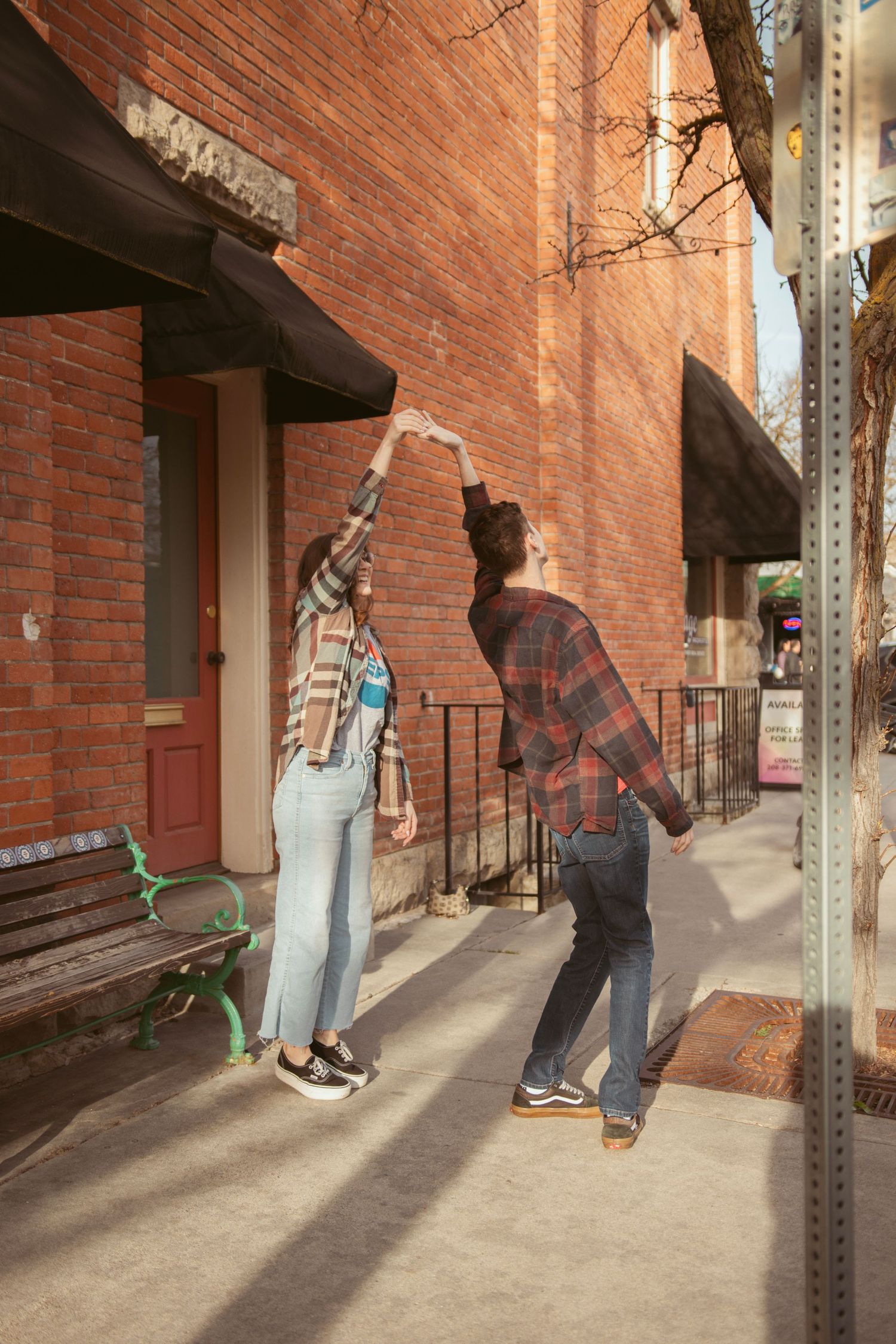 Two people dancing and having fun on a sidewalk by brick buildings.