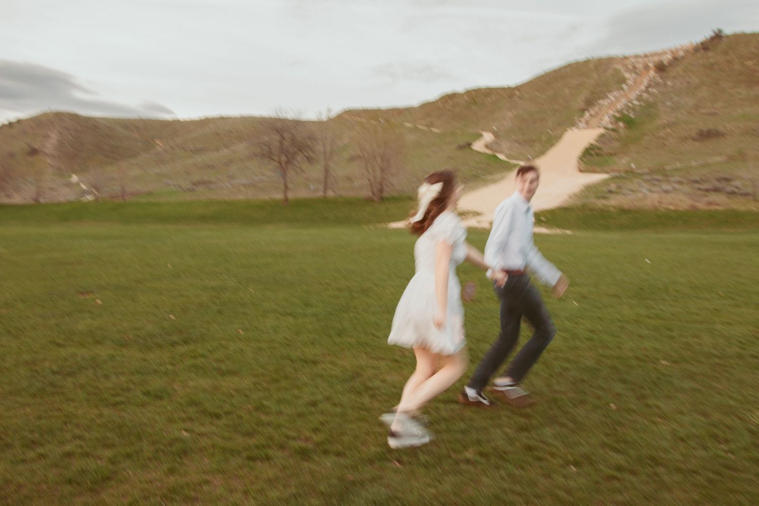 A couple runs and plays together across a green hillside during sunset.