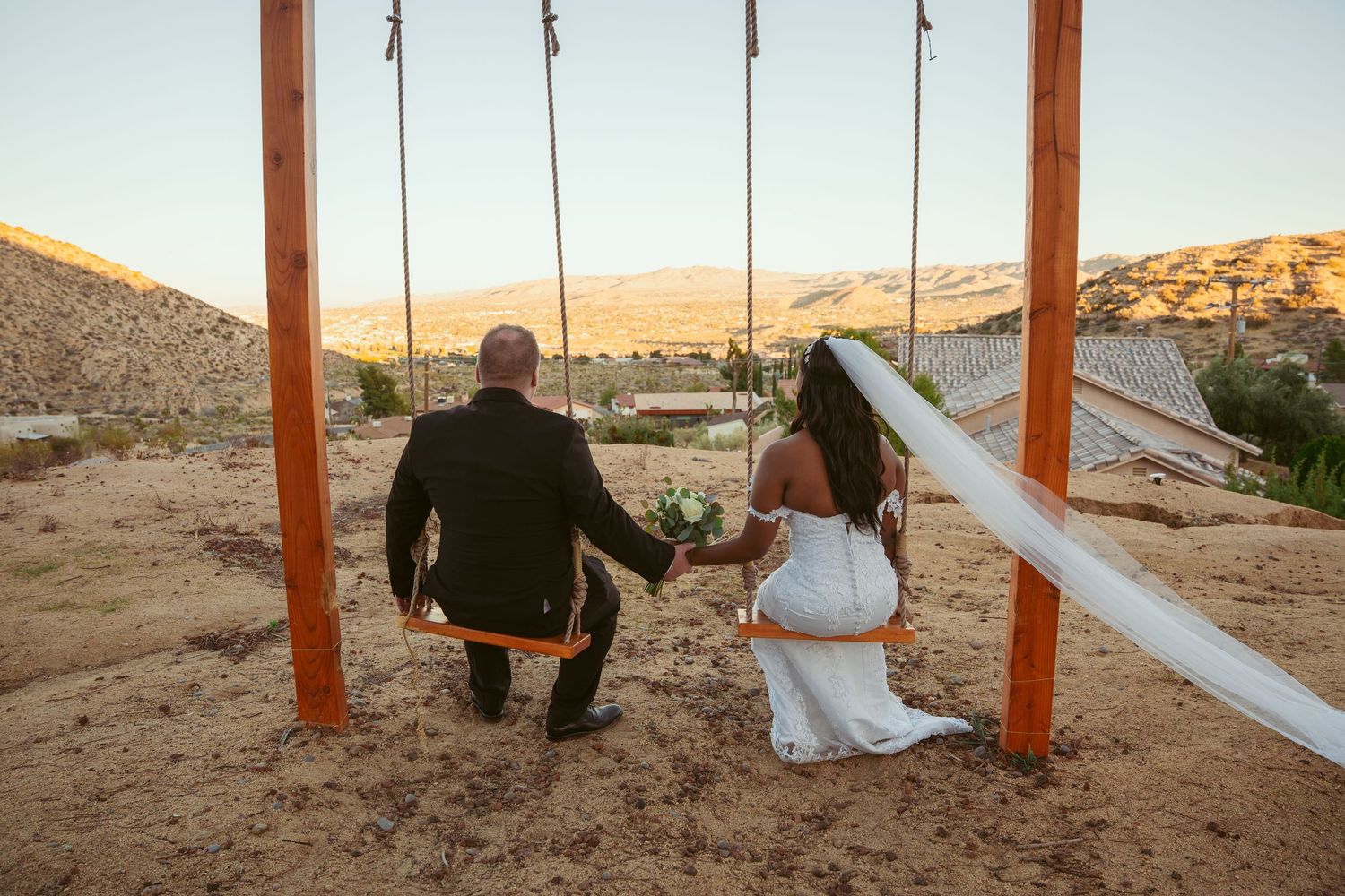 A couple enjoys romantic swings together in a desert setting with mountains in the background.