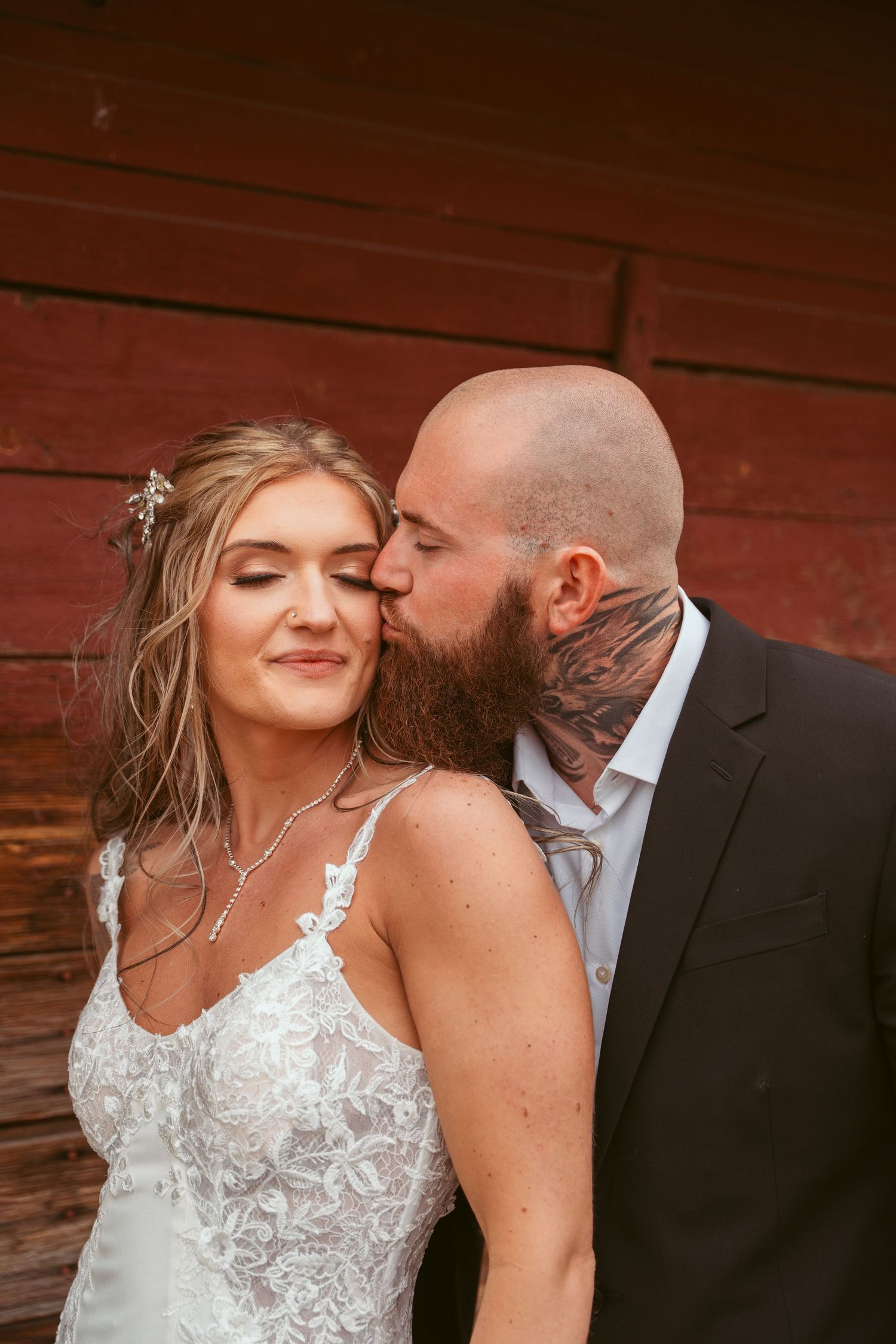 A couple shares an intimate moment against a rustic red barn backdrop.