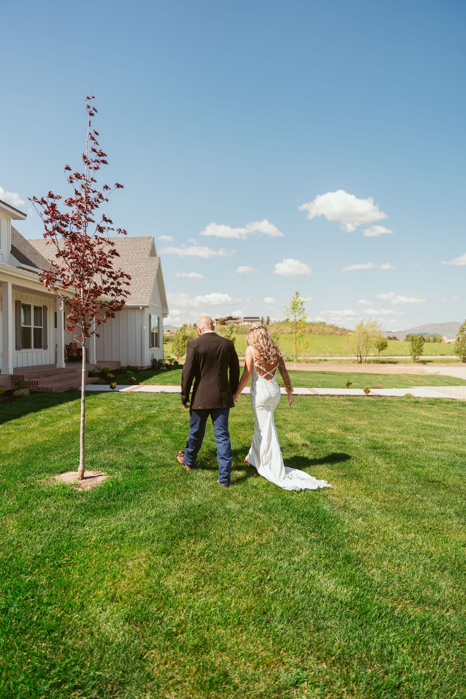 A couple walks away from their wedding ceremony across a green lawn with mountains in the distance.