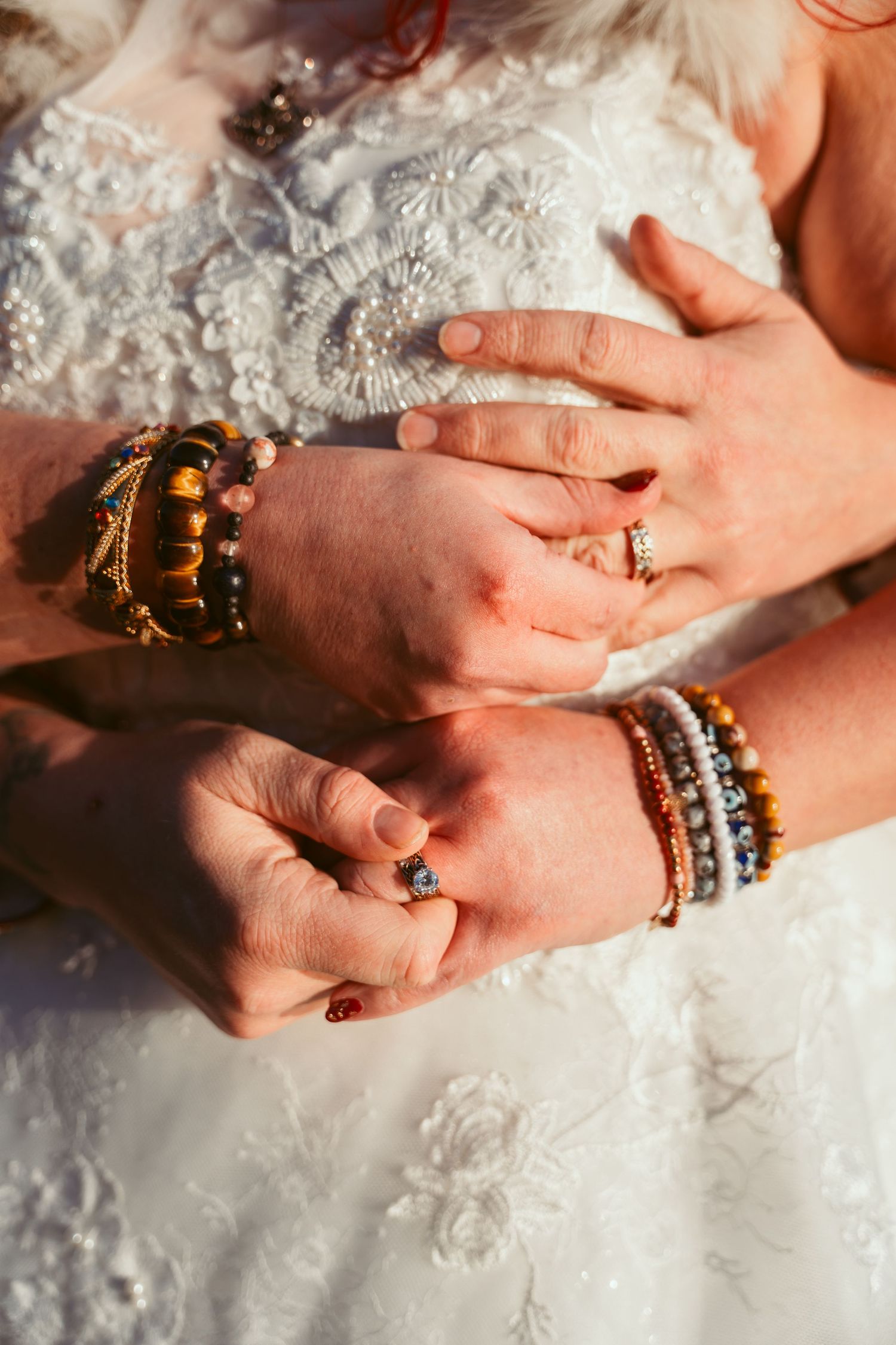 Close-up of hands wearing ornate jewelry and bracelets against white lace fabric.