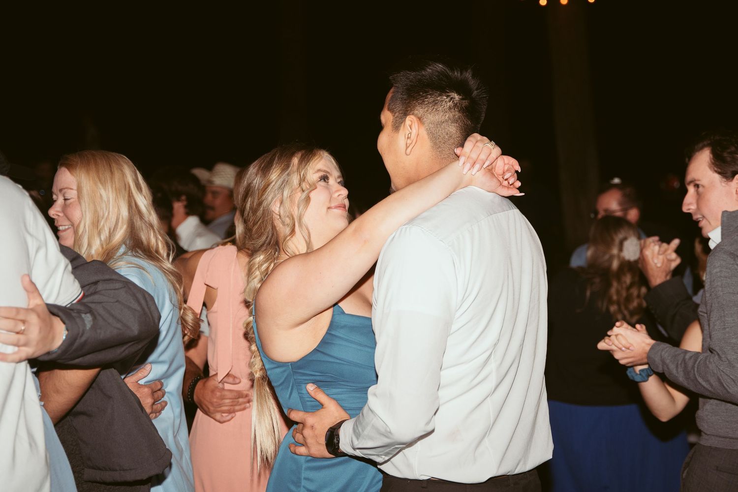Guests dancing and celebrating at a nighttime wedding reception under ambient lighting.