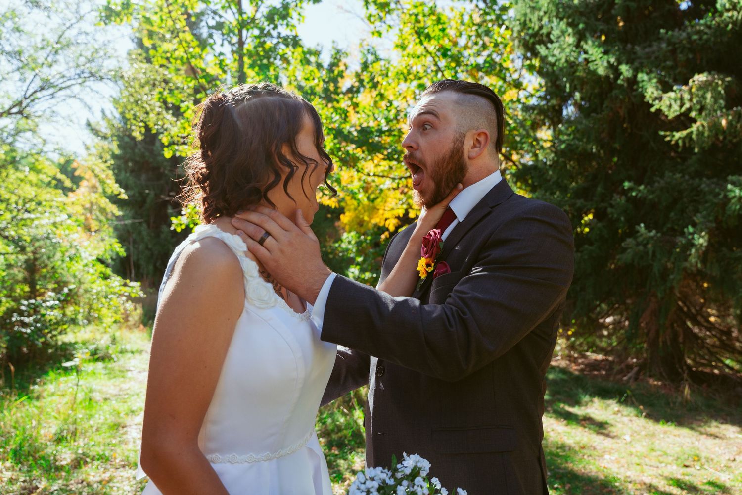 A candid wedding moment captured in bright sunlight with evergreen trees in the background.
