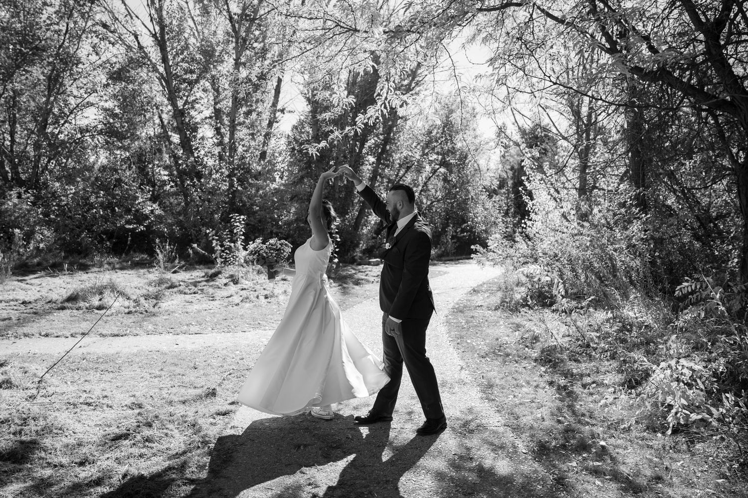 Black and white photo of a couple dancing on a wooded path during their wedding.