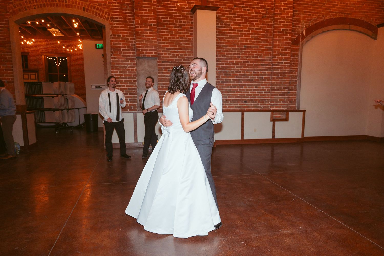 Wedding reception in spacious brick venue with string lights and hardwood floors.