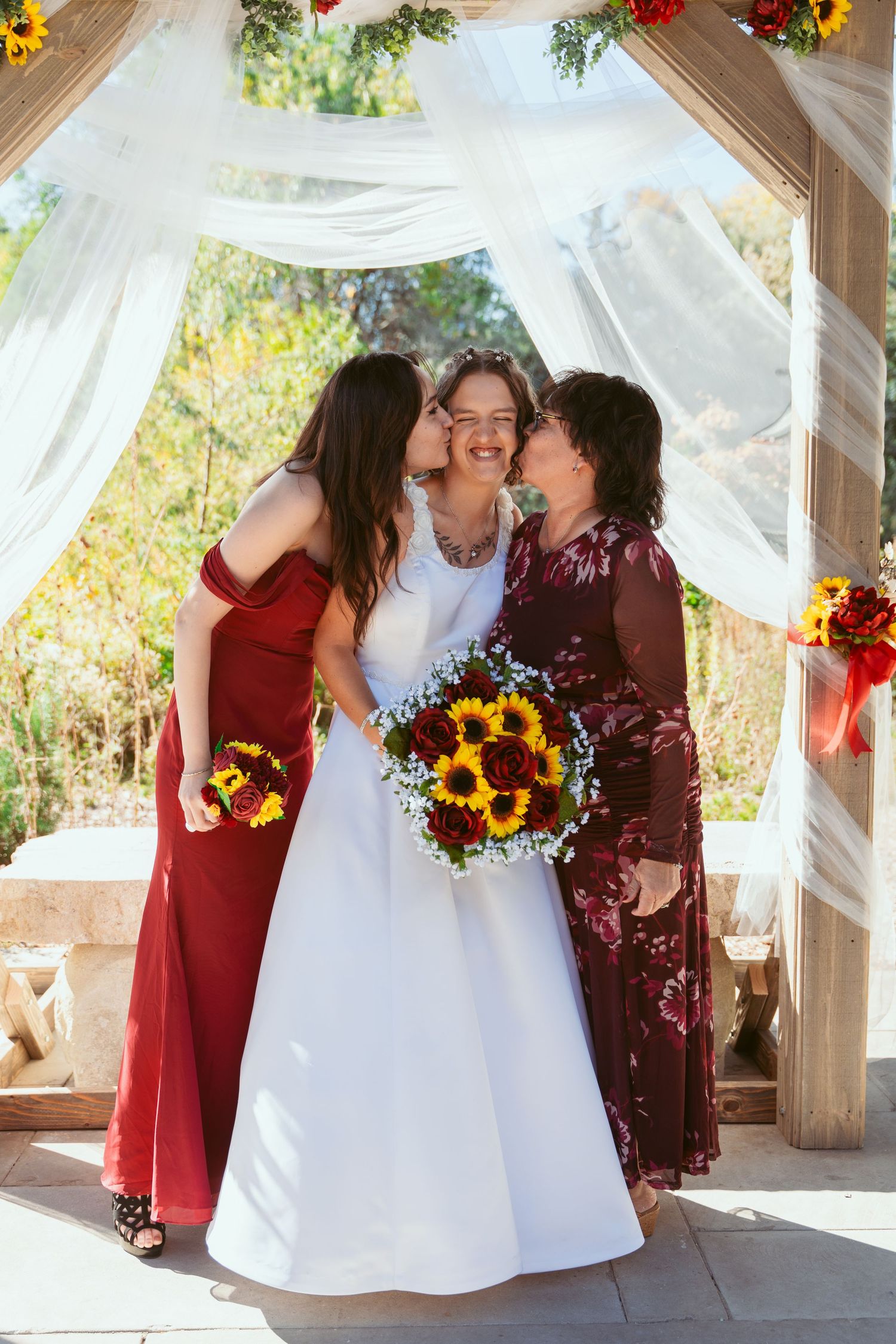 Wedding party shares intimate moment under white draped pavilion with autumn floral accents.