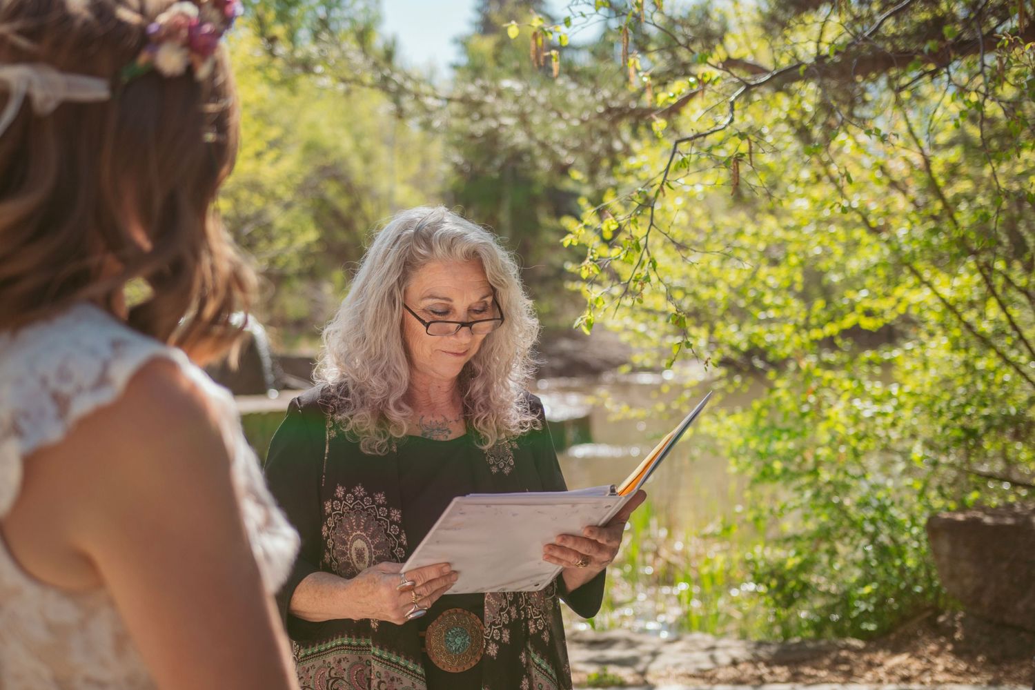 An outdoor wedding ceremony where an officiant reads from papers in a garden setting.