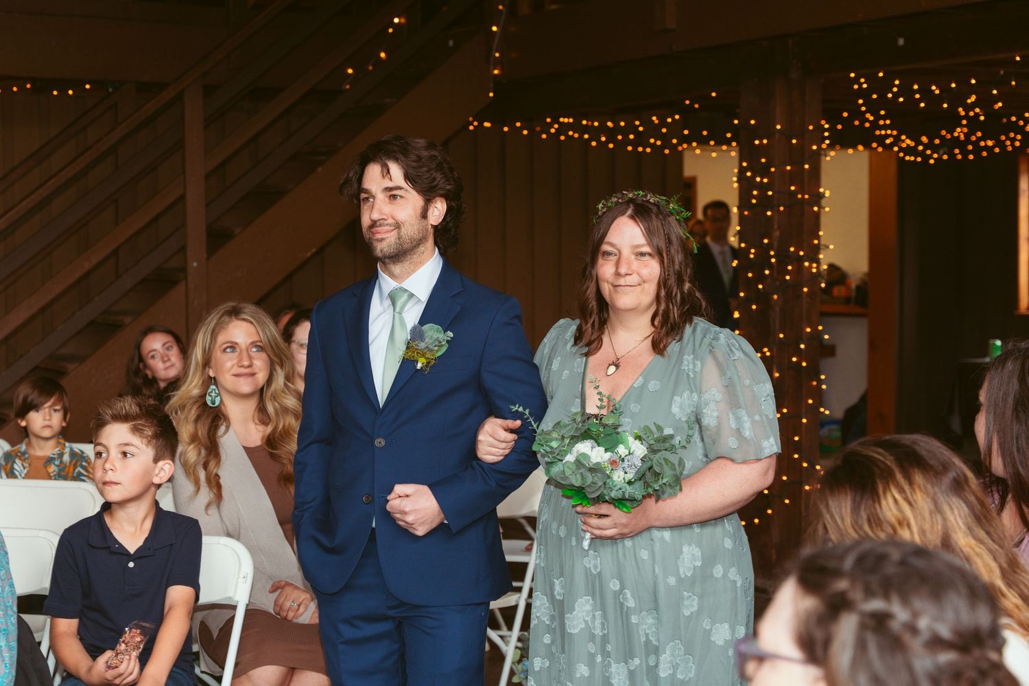 Festive gathering in a barn-style venue with decorative lighting and wedding guests.