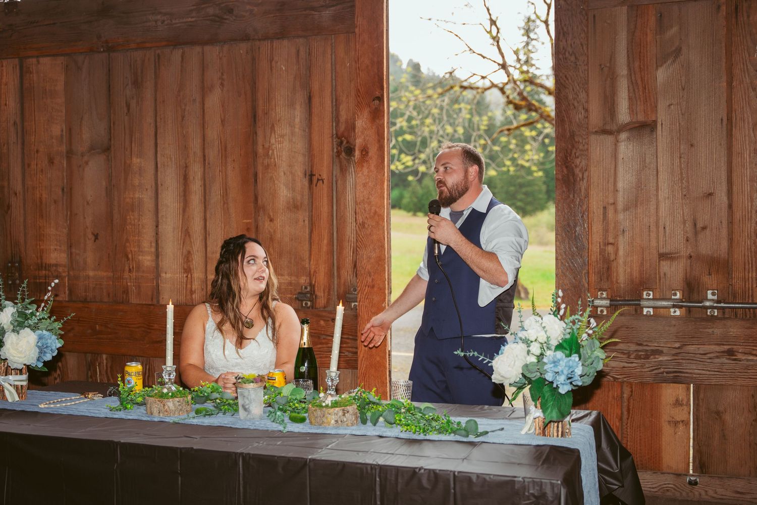Festive barn wedding reception with string lights and floral centerpieces on wooden tables.